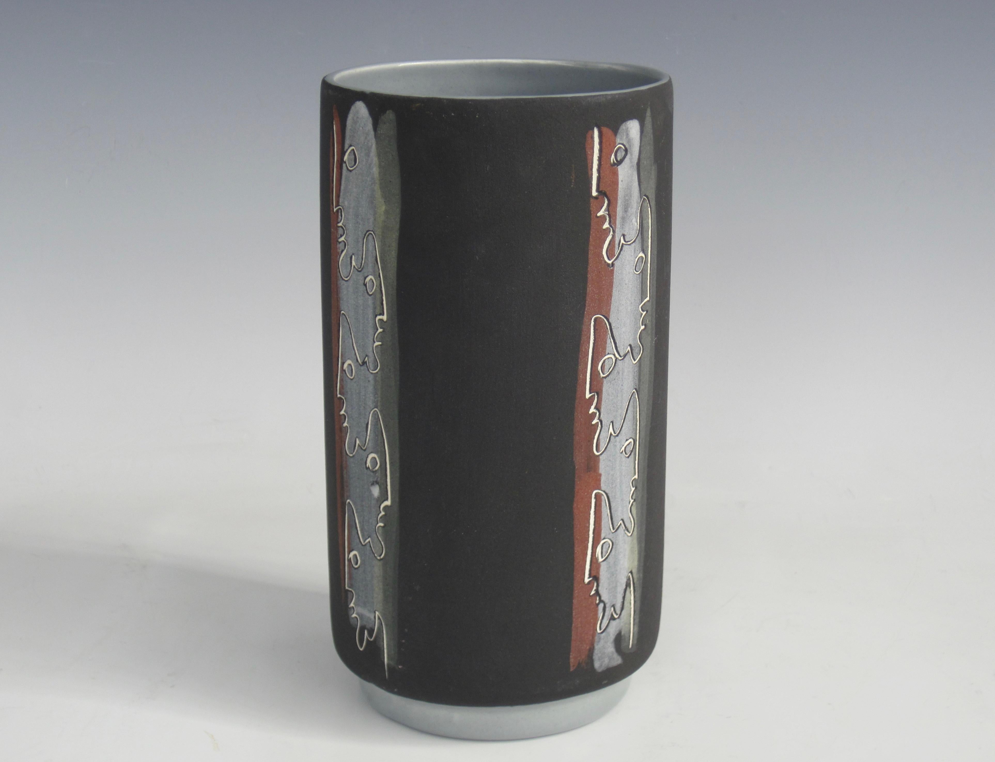 A mid-century tiki face vase by artist duo Charles and Alice Smith known as Chalice. This vase has alternating incised tiki silhouettes with brick red, gray and olive green vertical stripes on a coarse matte charcoal exterior. This interior is high