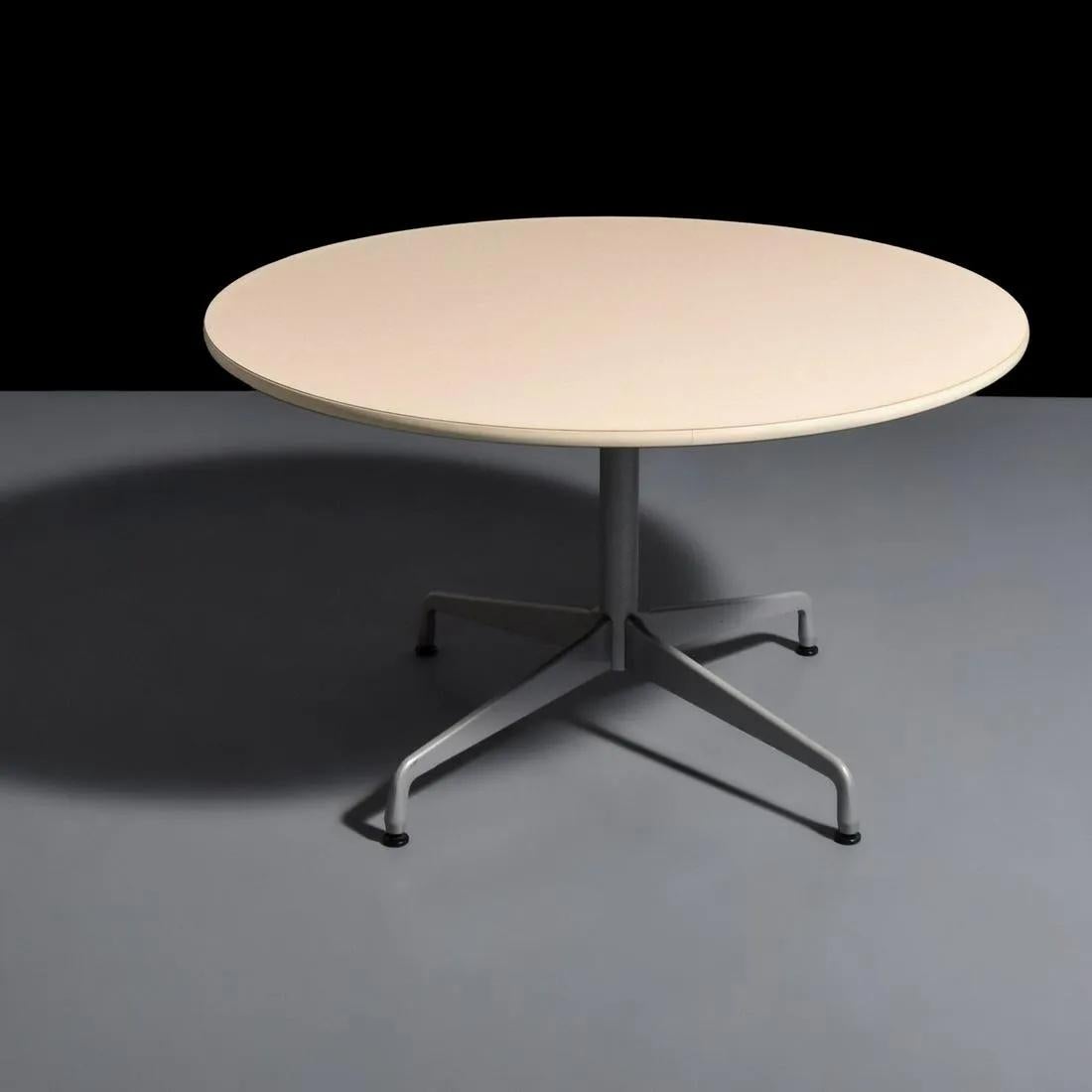 A timeless round dining or conference table designed by Ray and Charles Eames for Herman Miller. The table features a laminate top in white with light grey grain design standing on steel base. The base can be detached from the top and is nicely