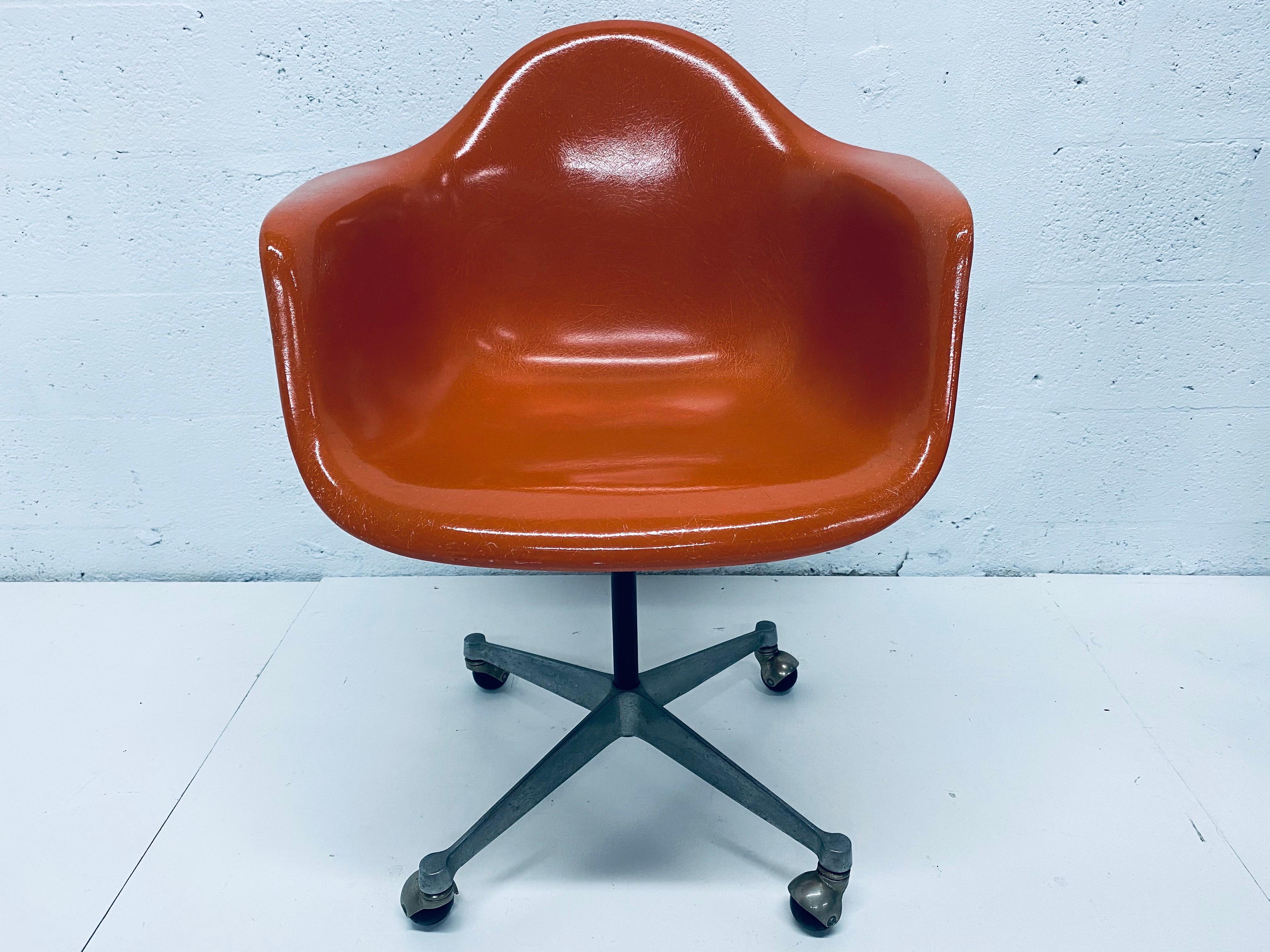 Original Charles and Ray Eames designed burnt orange moulded fiberglass desk chair on casters for Herman Miller, 1960s. Chair swivels smoothly. Not height adjustable.