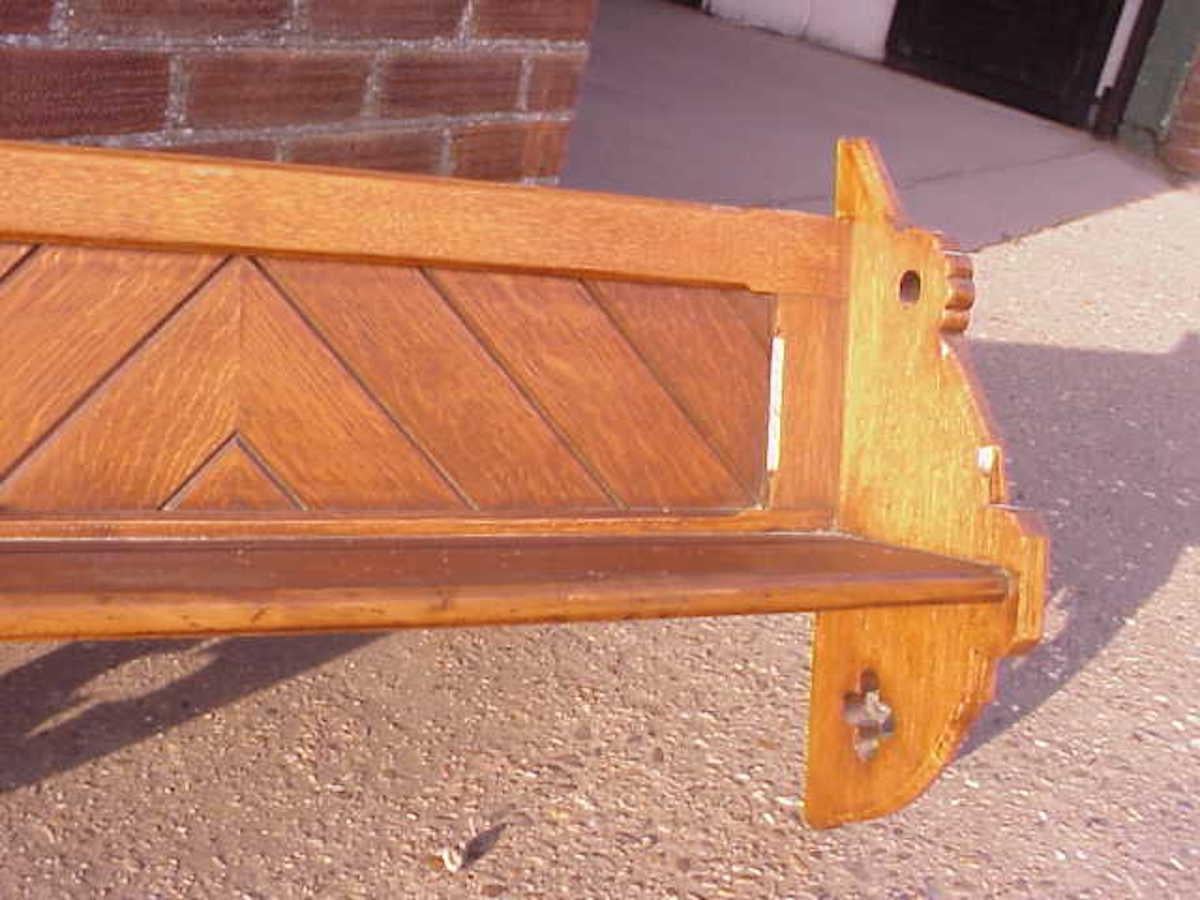 Charles Bevan, style of.
A Gothic Revival hanging oak shelf with exposed through tenon joints with crossed wedges to each of those joints, crisply cut trefoils and opposite decorative chevron boards to the back, with a small groove set back to the