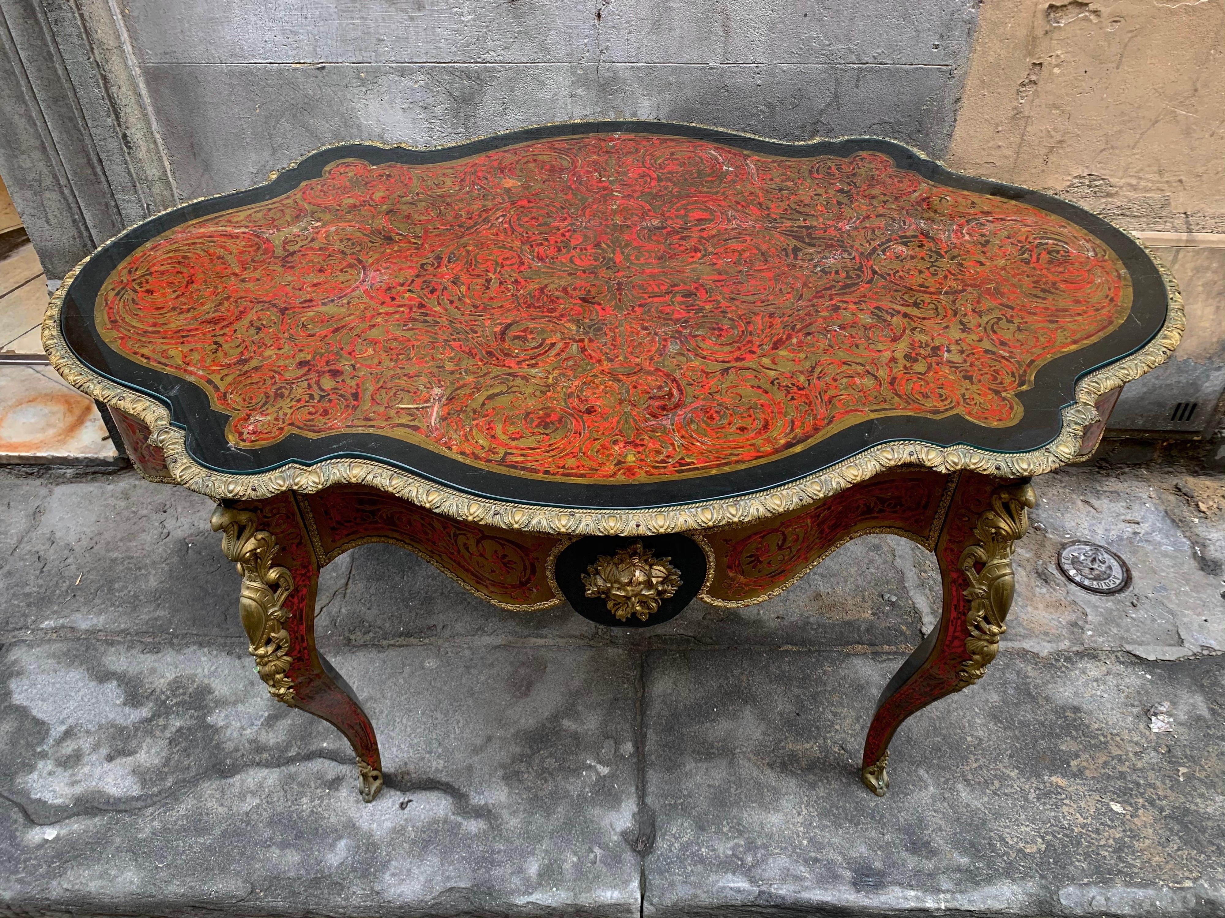 Charles- Boulle style ormolu-mounted tortoiseshell engraved brass and ebony finish desk.
Center or parlor table with serpentine-shaped top, inlaid with foliate brass scrollwork. Red and black painted frame with a central drawer, on shaped cabriole