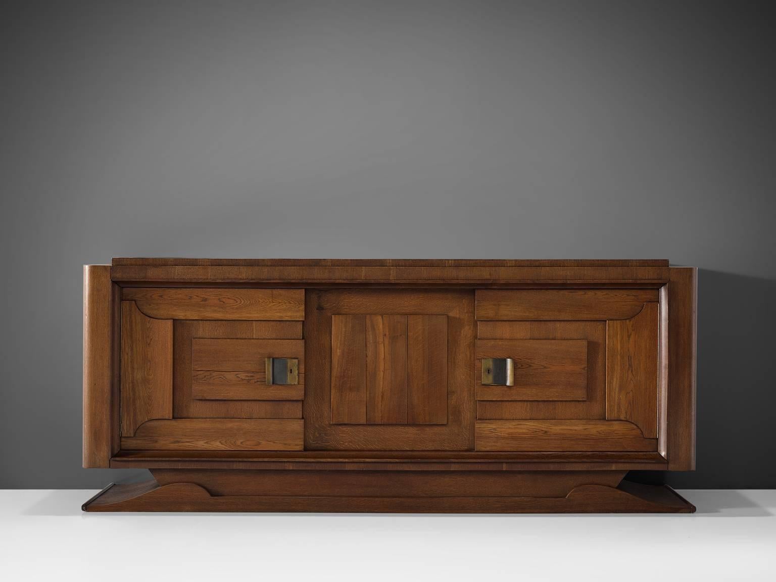 Charles Dudouyt, cabinet, oak and brass, France, 1930s. 

This French Art Deco oak credenza is designed by the decorator Charles Dudouyt. The dark stained oak frame gives this sideboard a sturdy character. The door panels show an interesting