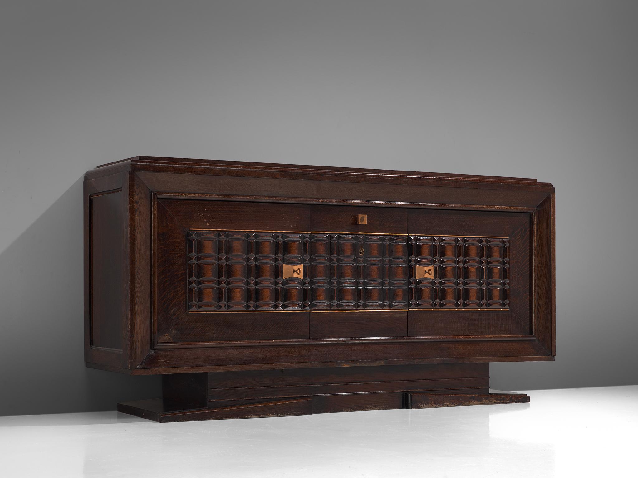 Charles Dudouyt, sideboard, darkend oak and copper, France, 1940

This sturdy credenza in oak is truly a sculptural piece. It is equipped with three doors hiding several shelves and a drawer which provide plenty of storage space. The detailing of