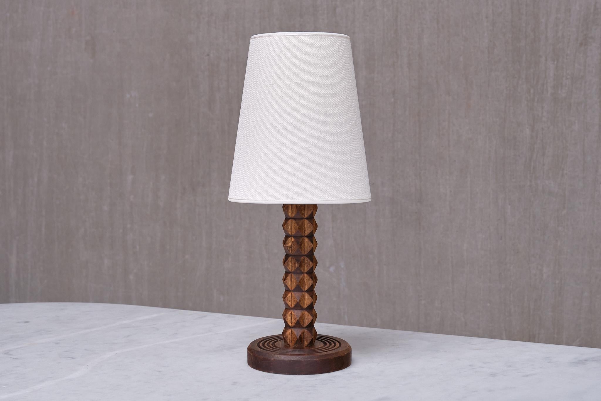 This rare and distinctive table lamp was produced in France during the 1950s. The rustic yet elegant design is attributed to the renowned French designer Charles Dudouyt. The carefully carved details of the wooden base and stem highlight the