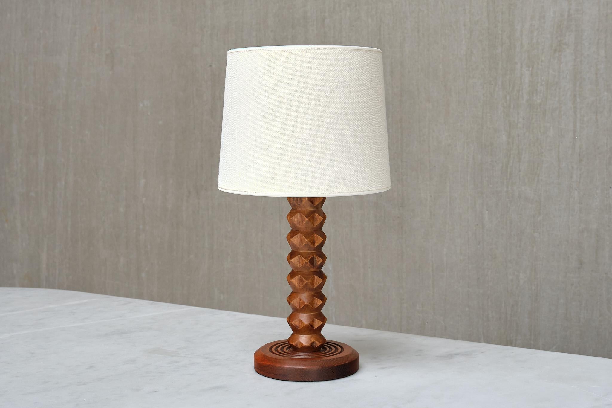This rare table lamp was produced in France during the 1950s. The rustic yet elegant design is attributed to the renowned French designer Charles Dudouyt. 

The carefully carved details of the wooden base and stem highlight the artisanal quality and