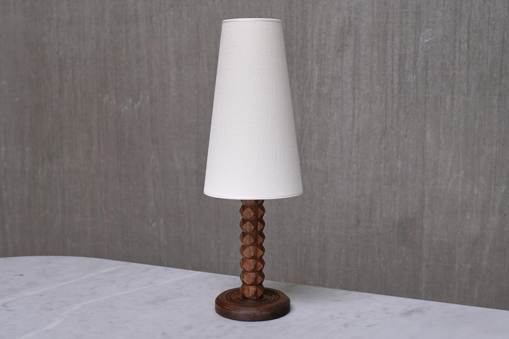 This rare table lamp was produced in France during the 1950s. The rustic yet elegant design is attributed to the renowned French designer Charles Dudouyt.  

The carefully carved details of the wooden base and stem highlight the artisanal quality