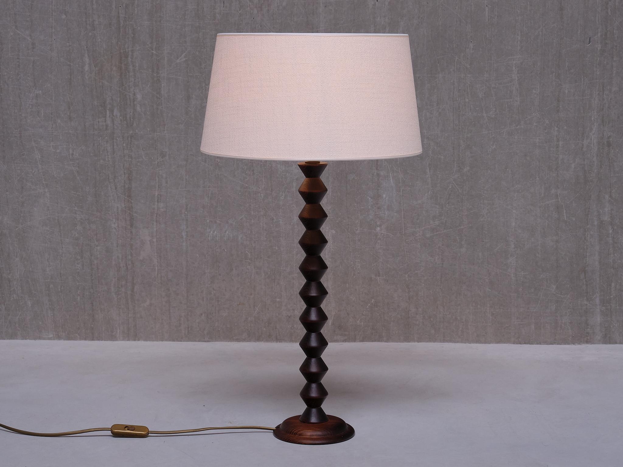 This striking tall table lamp was manufactured in France in the 1950s. The design is attributed to Charles Dudouyt. 

Crafted from dark stained oak wood, the lamp consists of a circular base and an intricately carved stem in a stacked disc shape.