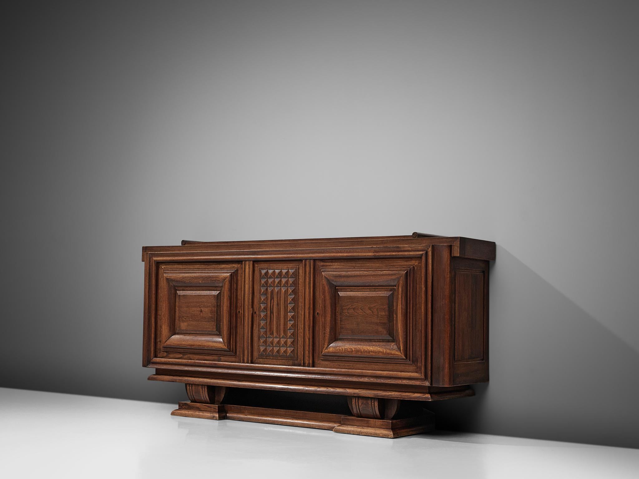 Charles Dudouyt, sideboard, darkened oak, France, 1940.

Sturdy credenza in oak that is truly a sculptural piece. This three-door sideboard is equipped with several shelves that provide plenty of storage space.  The graphic, rhythmical door panel