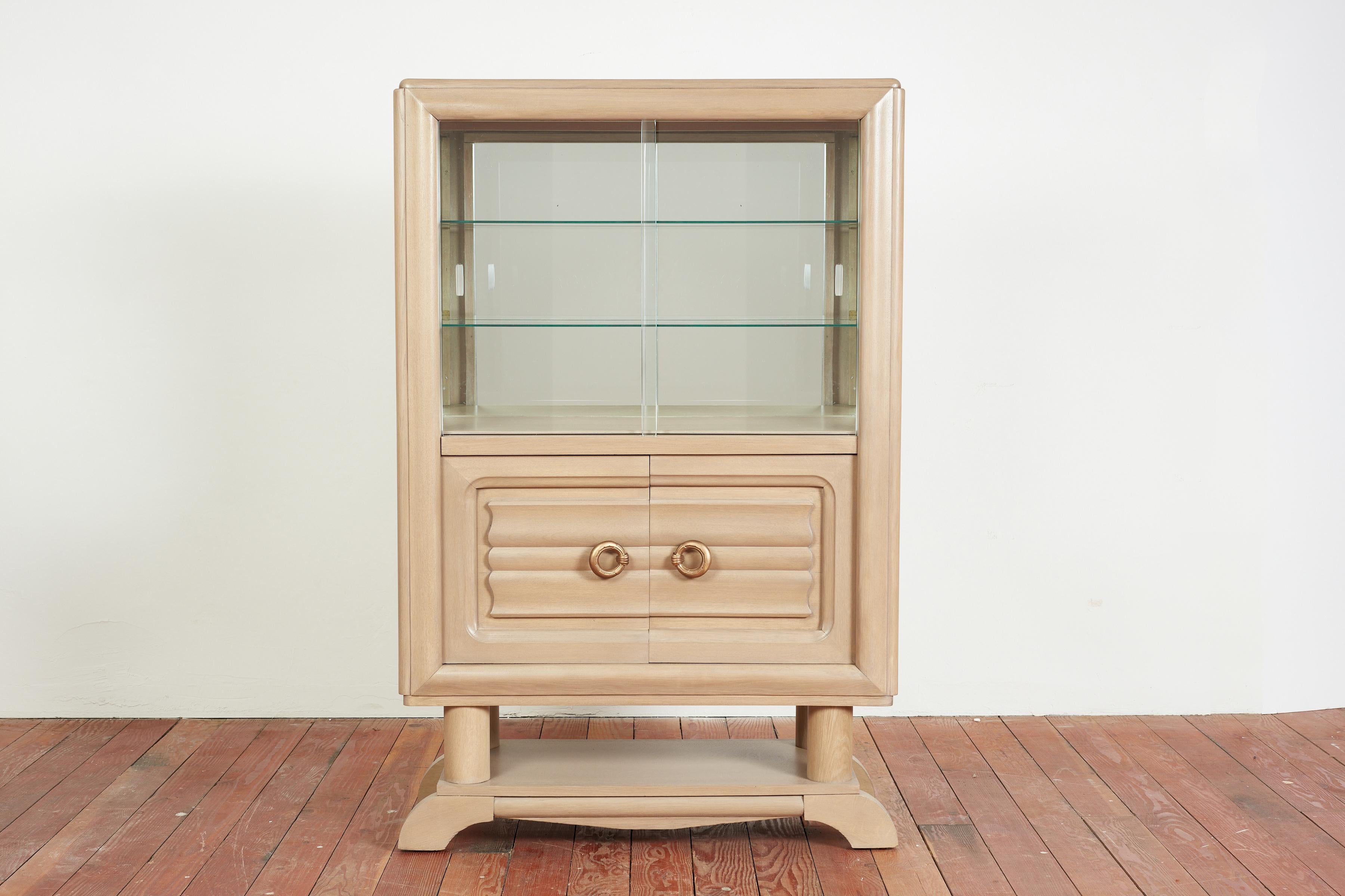 Charles Dudouyt vitrine with glass upper sliding doors and interior mirror with 2 glass shelves. 

Lower doors are carved with signature Dudouyt pattern and open to reveal interior shelving with inlay detail. 

Large cast brass circular hardware