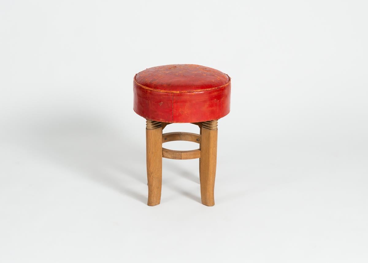 Round polished-oak and red leather stools by French designer Charles Dudouyt.