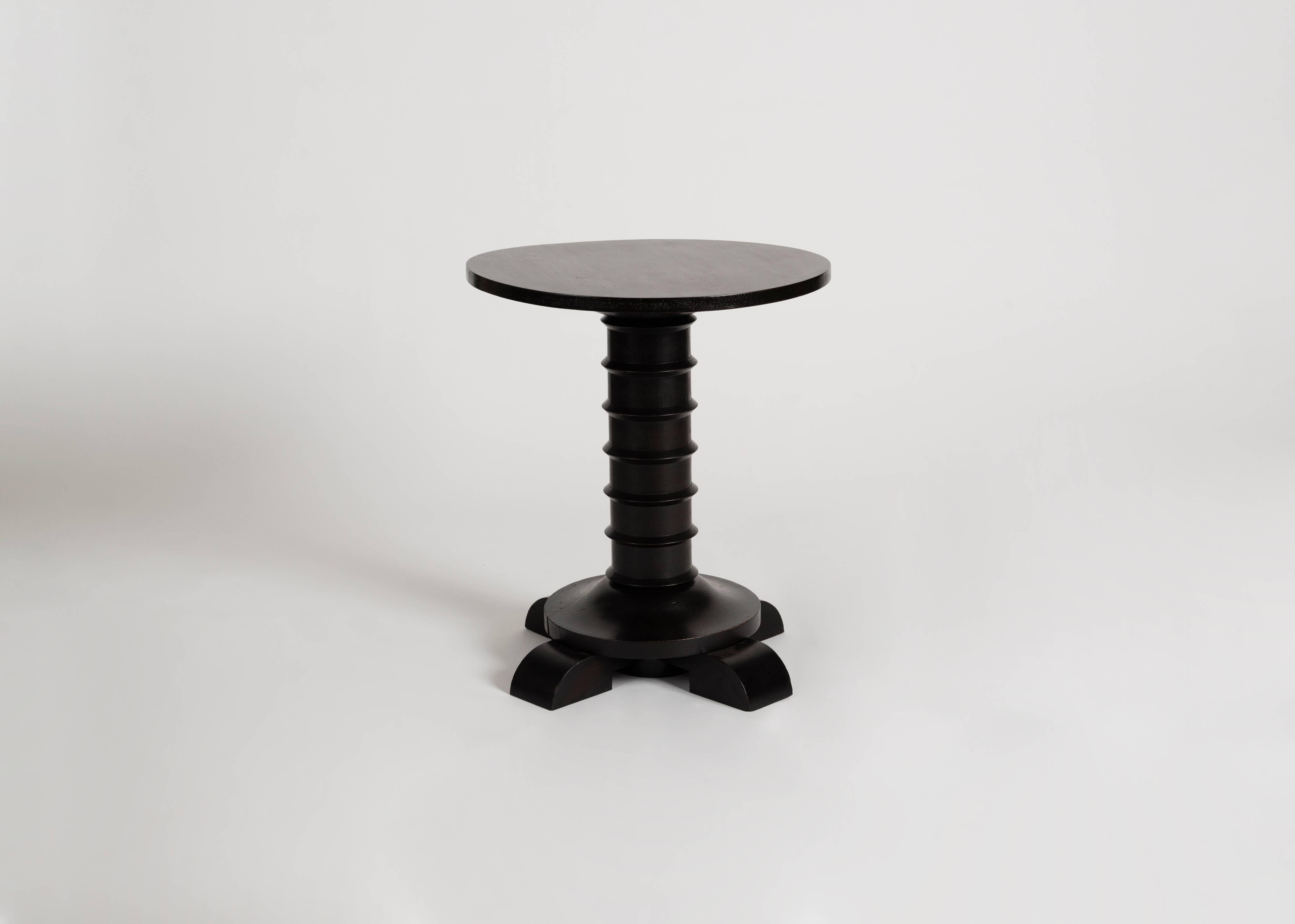 This table in blackened wood by Charles Dudouyt possesses a round, flat top and four stout legs, upon which rests a cylindrical body accented with well-spaced horizontal bands.