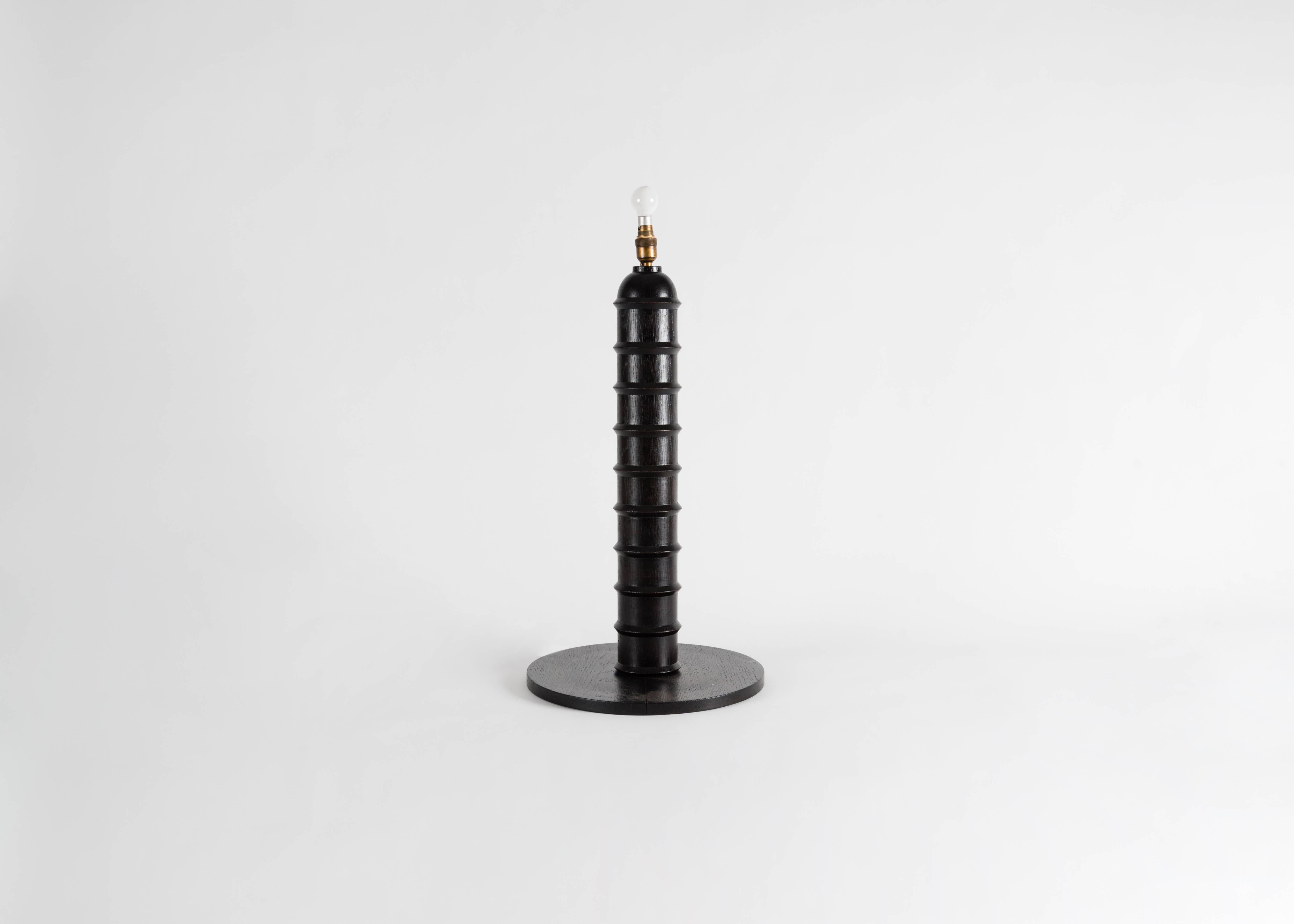 This lamp in blackened wood by Charles Dudouyt possesses a round, flat base and a cylindrical, towering body accented with well spaced horizontal bands.