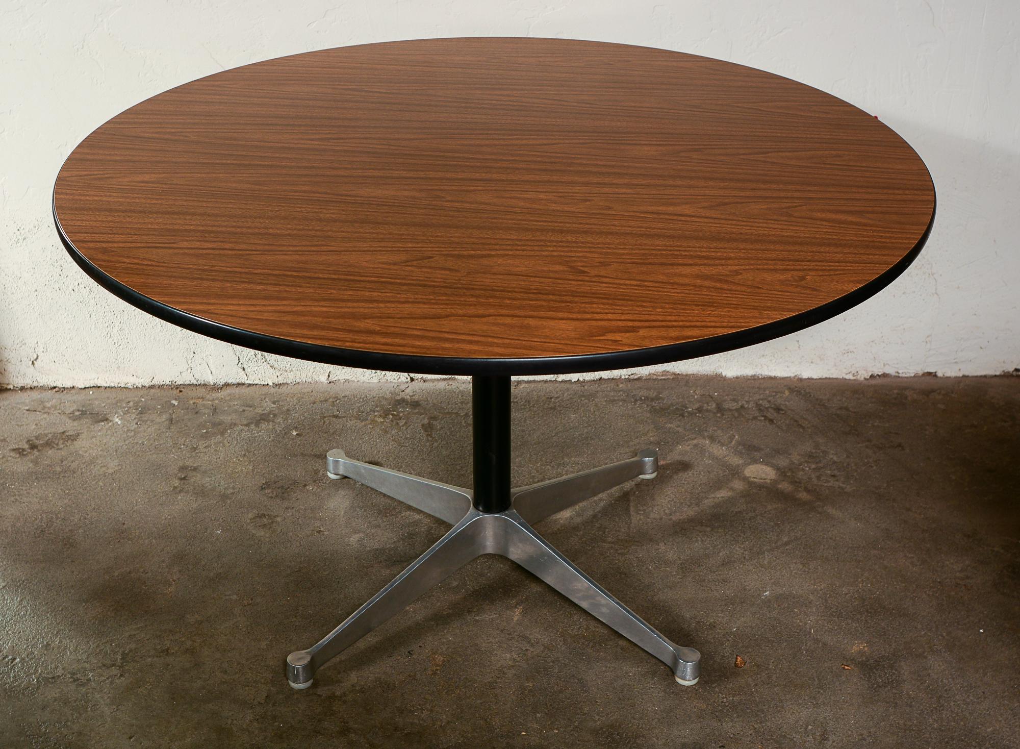 Contract base dining table by Charles and Ray Eames. This table has the earlier aluminum group base. The top is a faux wood grain laminate. The table has the round black medal label. There is a little wear to the rubber edge. The aluminum base has