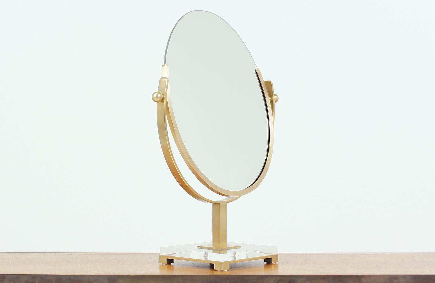 Dazzling brass mirror designed by Charles Hollis Jones in the United States circa 1970s. This beautiful double-sided oval mirror maintains all its original components, including the lucite base, brass hardware and both mirrors. The brass has been