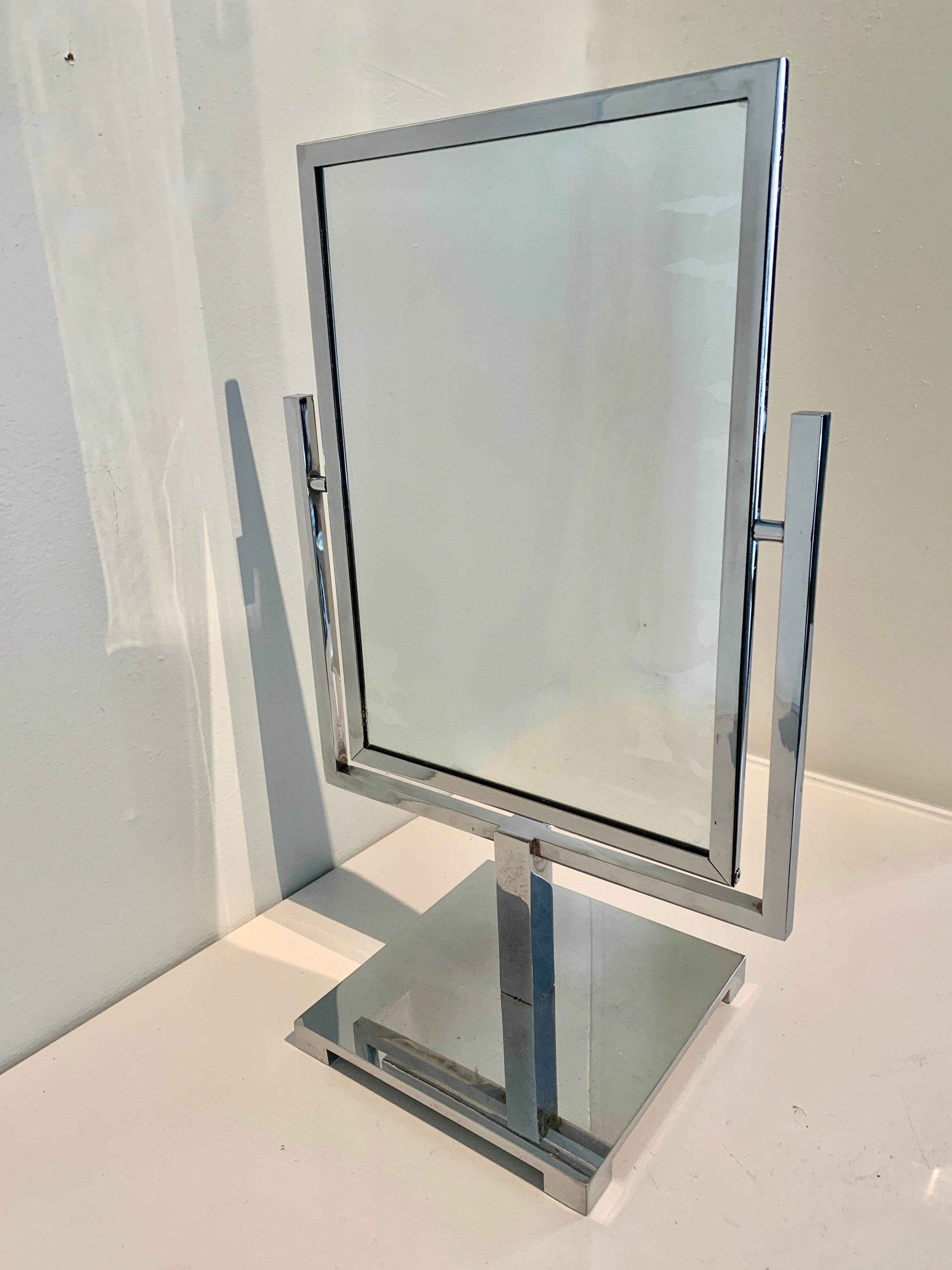 Un merveilleux miroir architectural. Le miroir est double face avec une réflexion normale (non grossissante) des deux côtés. Le miroir est enchâssé dans un cadre en chrome poli et repose sur un support du même matériau - quatre petits pieds.