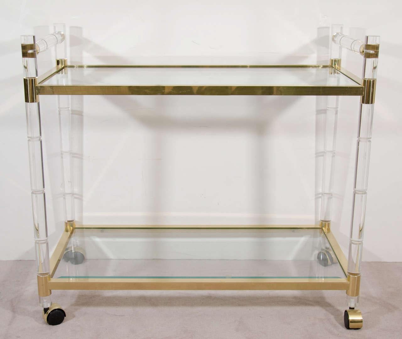 Bold but sleek, this brass-and-Lucite rolling cart designed by Charles Hollis Jones for his 'Regency Bamboo' line. Featuring faux-bamboo Lucite rails, brass frame with clear glass shelves. Casters ensure this sophisticated bar cart is every bit as