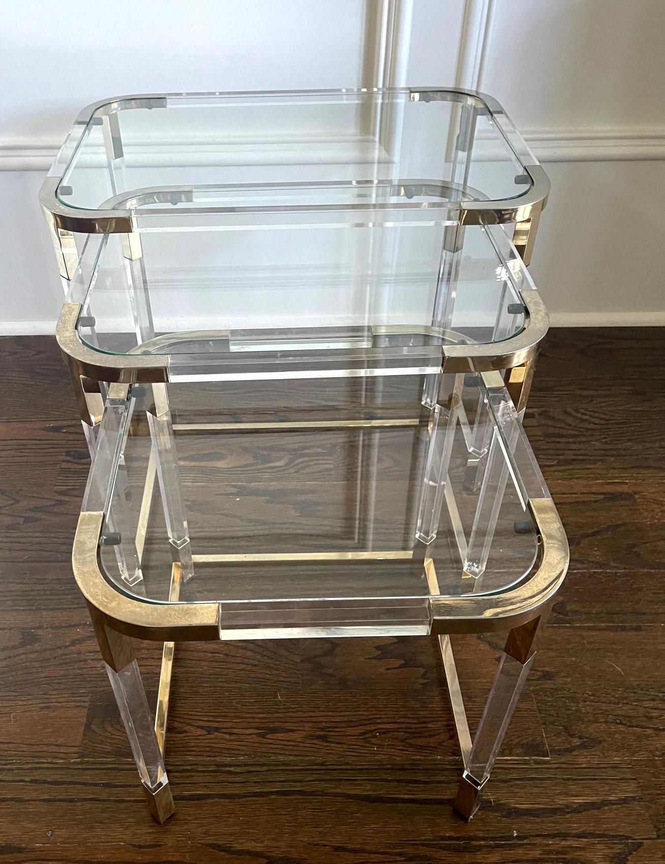 A set of three nesting tables by Charles Hollis Jones circa 1970s. The metric line employs Lucite frame construction with brass corner bracket joints to showcase a modern linear silhouette. The top surfaces are glasses. These nesting tables are