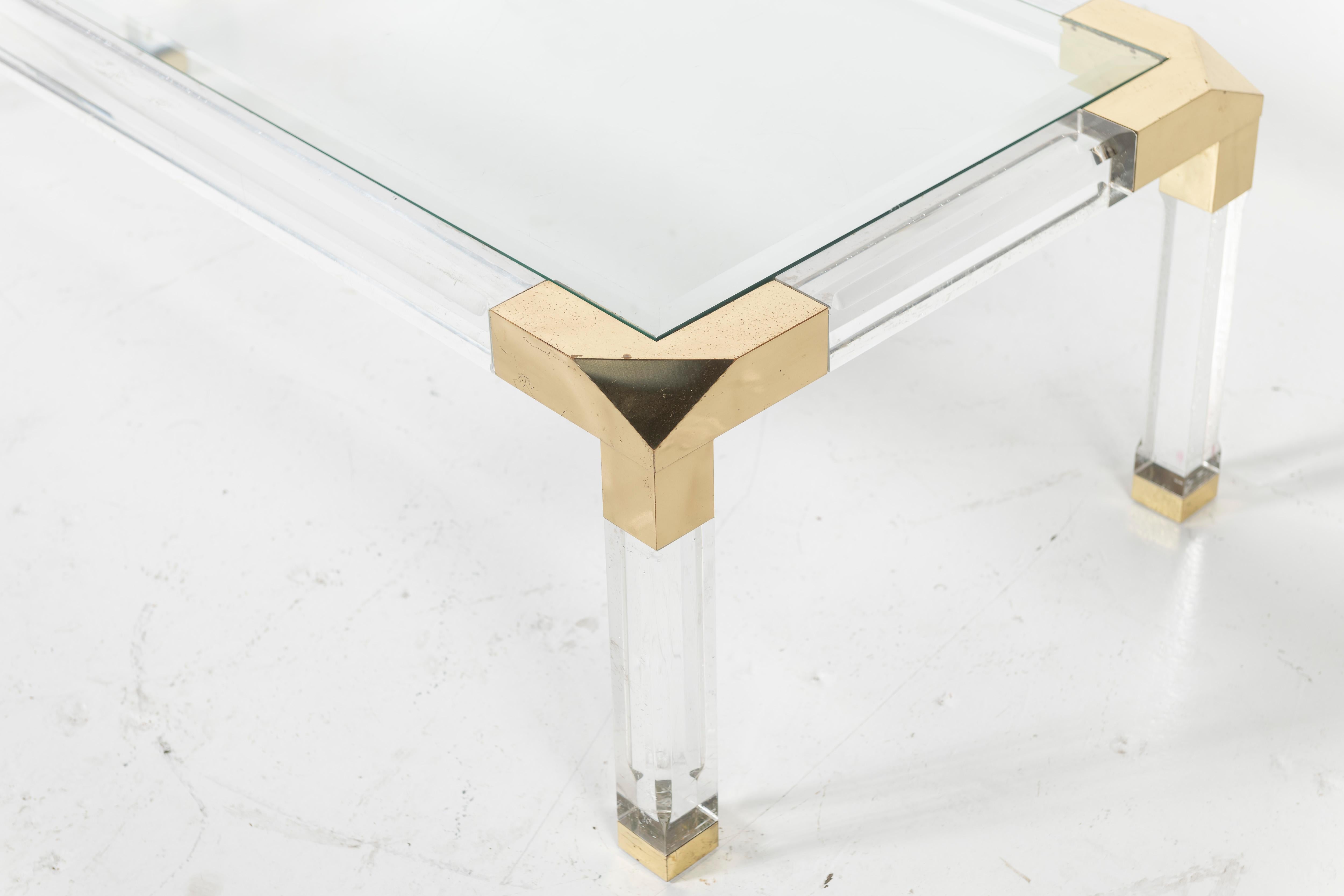 Dieser rechteckige Couchtisch im Stil von Charles Hollis Jones besteht aus Lucite und Acryl mit einer Tischplatte aus Glas mit Messingverzierungen. Die schweren und dicken Lucite-Beine und der Rahmen halten die Glasplatte.

 