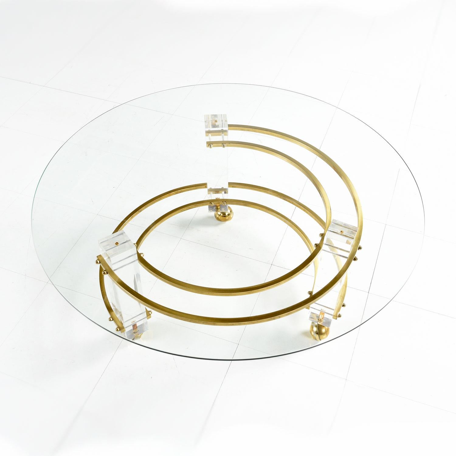 Spectacular vintage Hollywood Regency Lucite coffee table in the style of Charles Hollis Jones. The glass top has a rounded silhouette mimicking the dynamic contours of the table base. Staggered, semi-circle brass spanners convex at the bottom and