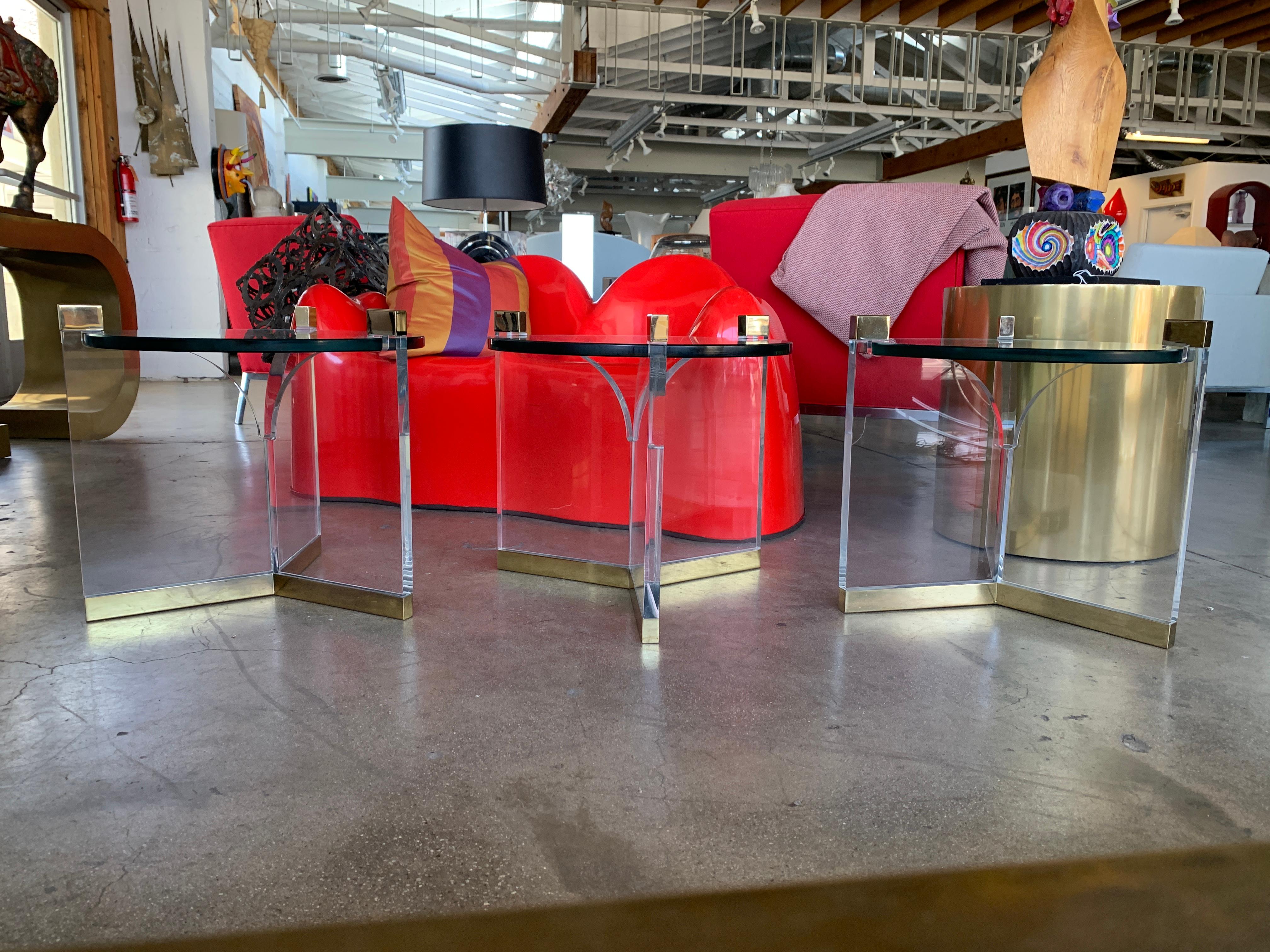 A set of 3 Charles Hollis Jones trefoil tables in brass, Lucite and glass. These are vintage tables, not new production. The glass top diameter alone is 20 inches and measuring taking into account the ends it is 22 1/2 inches in diameter. The brass