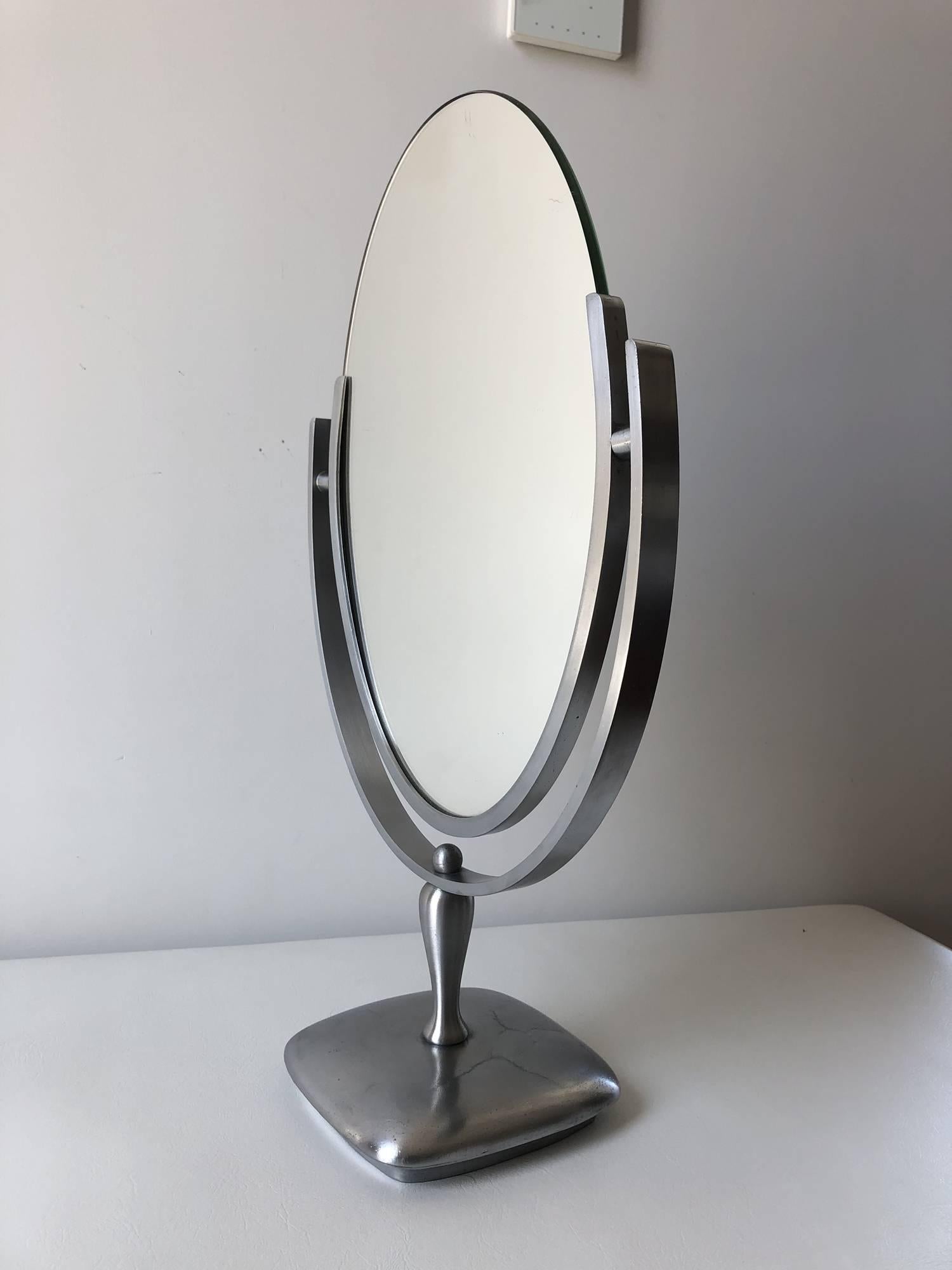Beautiful oval mirror designed and manufactured by Charles Hollis Jones in the 1960s. The mirror has a satin metal frame and base, the mirror has a beveled finished and is in excellent condition.

The piece is signed and dated by the