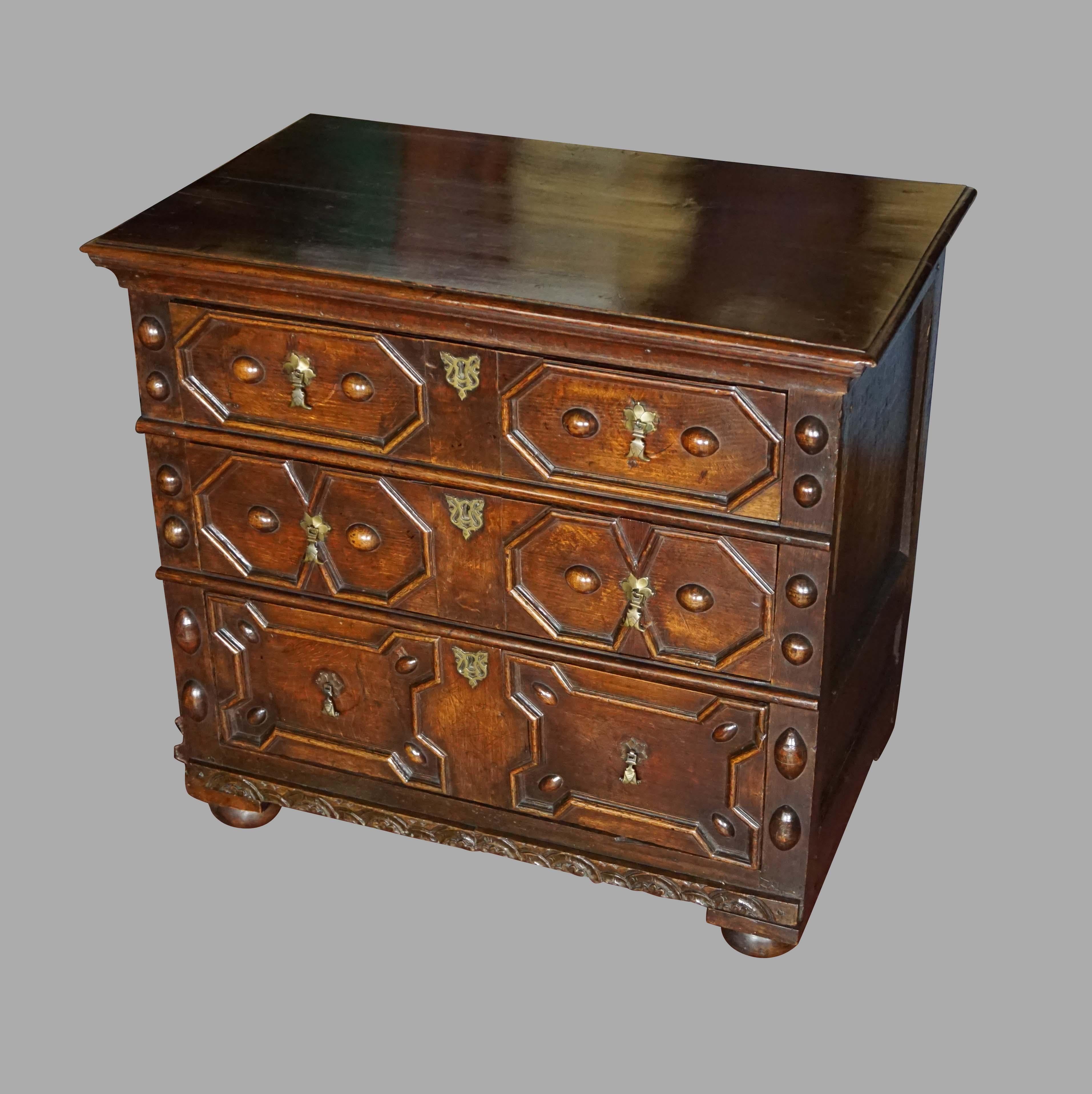 An English Charles II period oak 3-drawer chest, the top with moulded edge over 3 drawers with geometric mitre moulded fronts, with brass teardrop pulls and paneled sides resting on replaced bun feet. The drawer sides and bottoms retaining most of