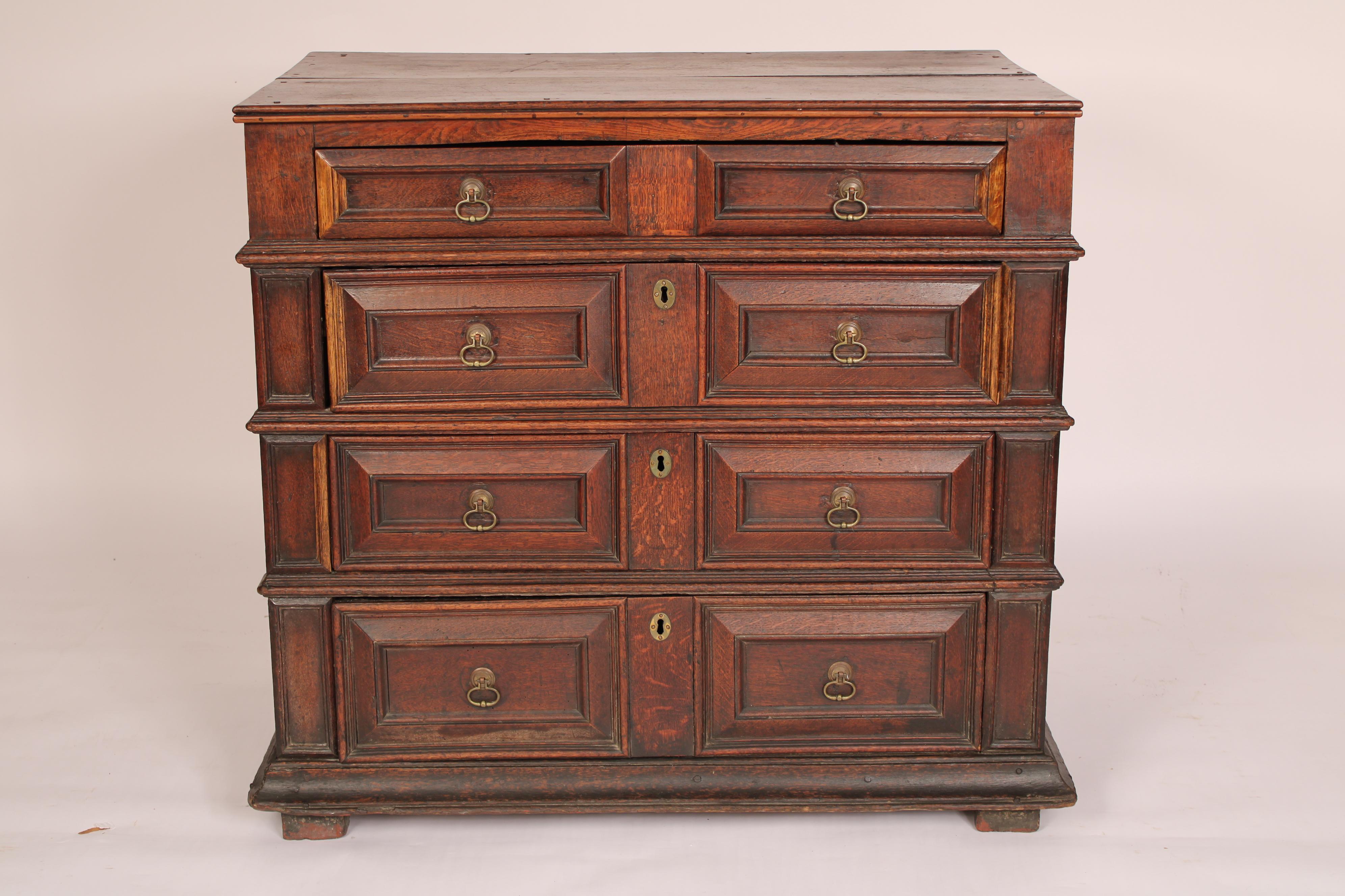 Charles II / Jacobean oak chest of drawers, 17th century. With a two board top with molded front and side edges, 4 drawers with molded edges and brass hardware, paneled sides resting on square feet. The feet are a continuation of the right and left