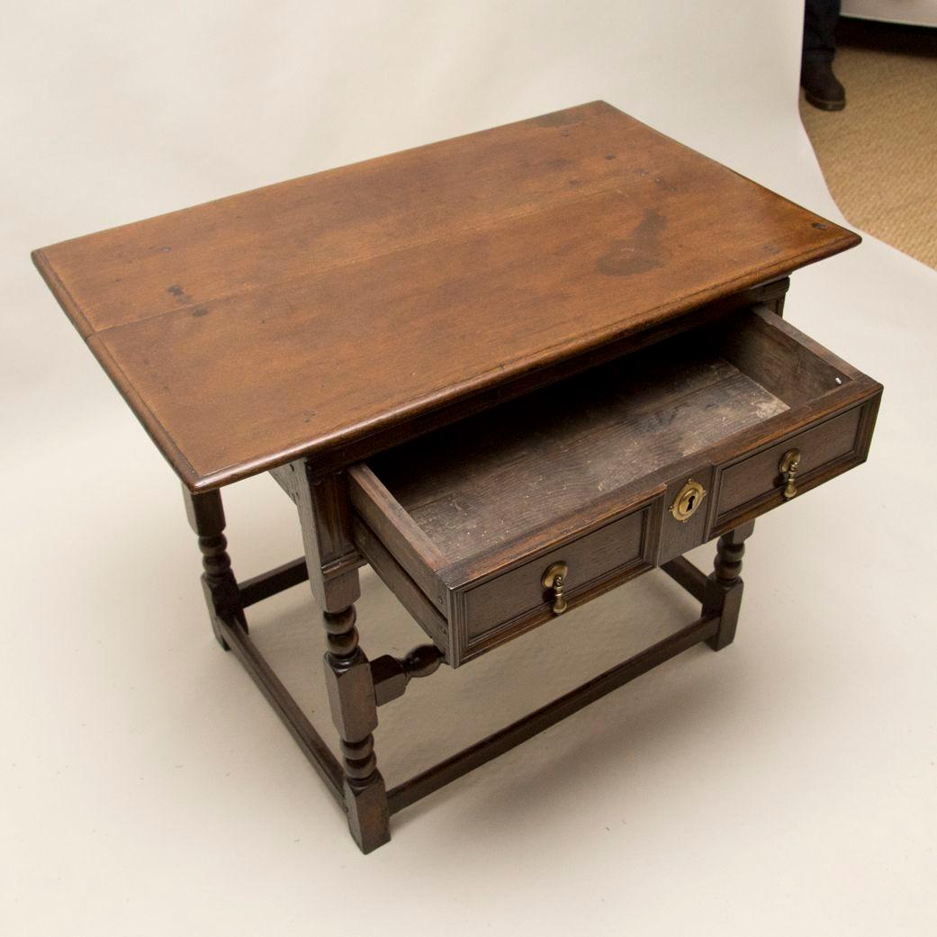 ?Good English 17th century oak side table, the two plank top having thumb molded edge, over single drawer with geometric panels surrounded by applied fruitwood bosses and cabochons, over heavy thumb molded support, standing on bobbin turned legs