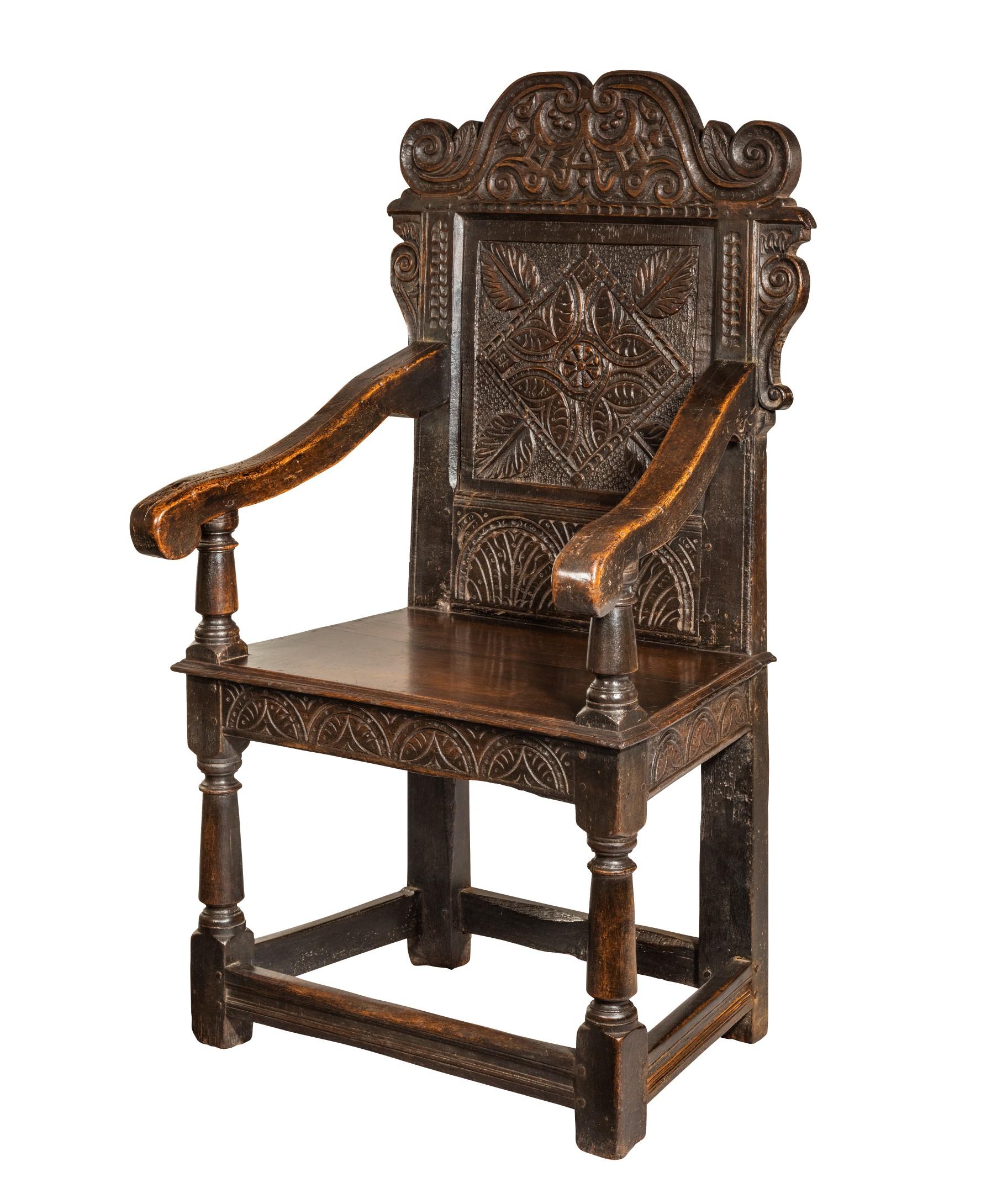 A superb Charles II Yorkshire carved oak armchair; the armchair's scrolling cresting rail carved with thistles and stylised foliage above scrolling ear pieces and downswept arms which flank a panelled back boldly carved with central diamond