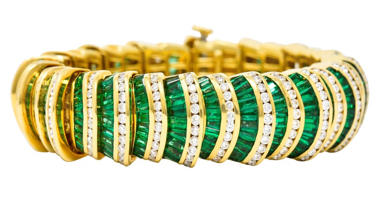 Considerable bracelet is comprised of fanned gold links that fit into one another to create a perpetual scale-like profile motif. Each set with a channel of round brilliant cut diamonds with a channel of emeralds. Total diamond weight is