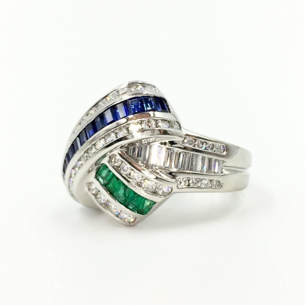 A sophisticated and artistic design. This signed Charles Krypell criss-cross X design ring consists of polished platinum with perfectly set channels of blue sapphires and emeralds giving it a modern and sleek aesthetic. High quality gemstones that