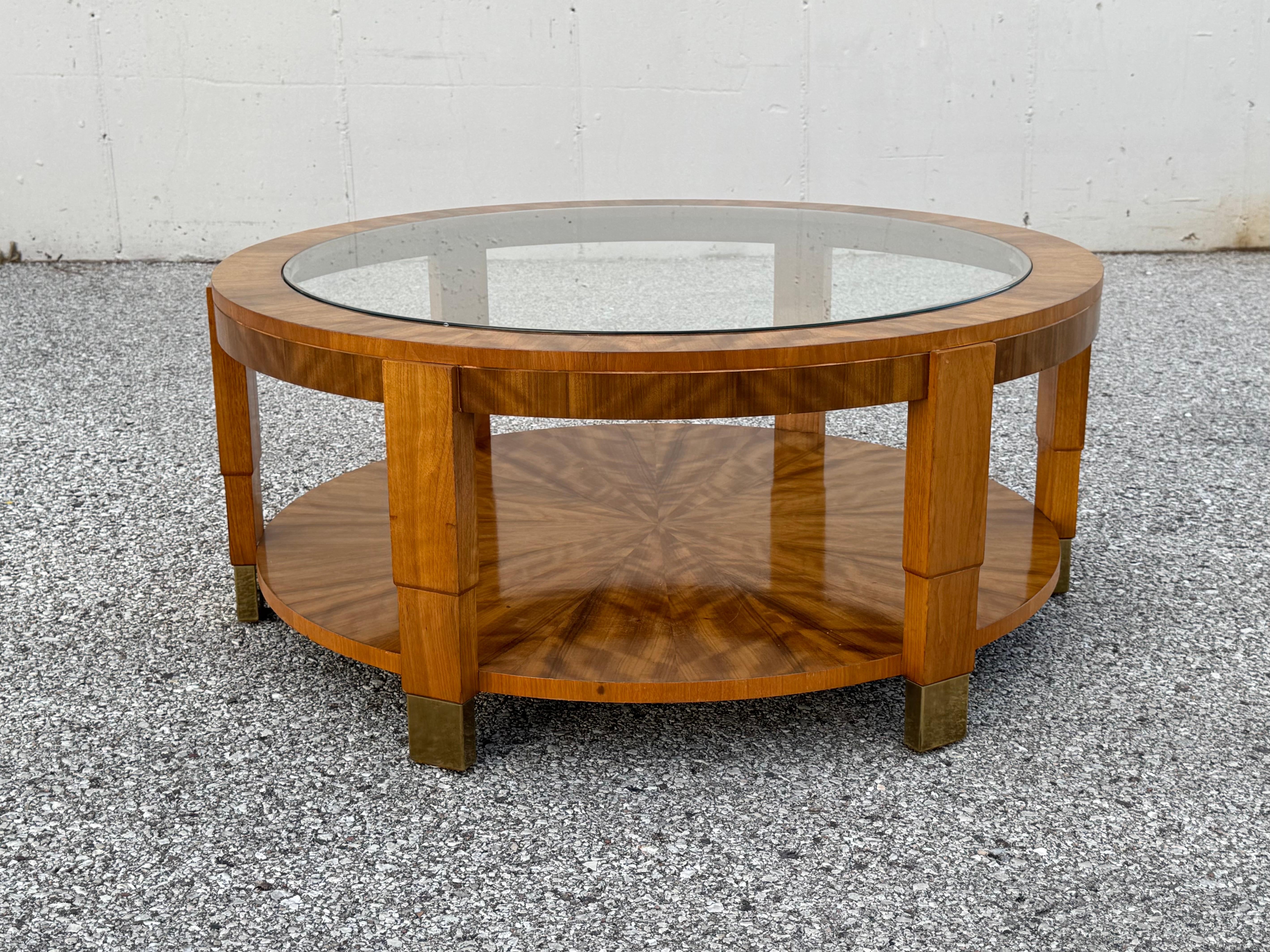 Attributed to designer Charles Pfister, this 1980s High Style Art Deco inspired round glass top coffee table in exotic flame wood veneer with stepped down designed legs, capped off with brass sabots. Unmarked, possibly custom, in the style of