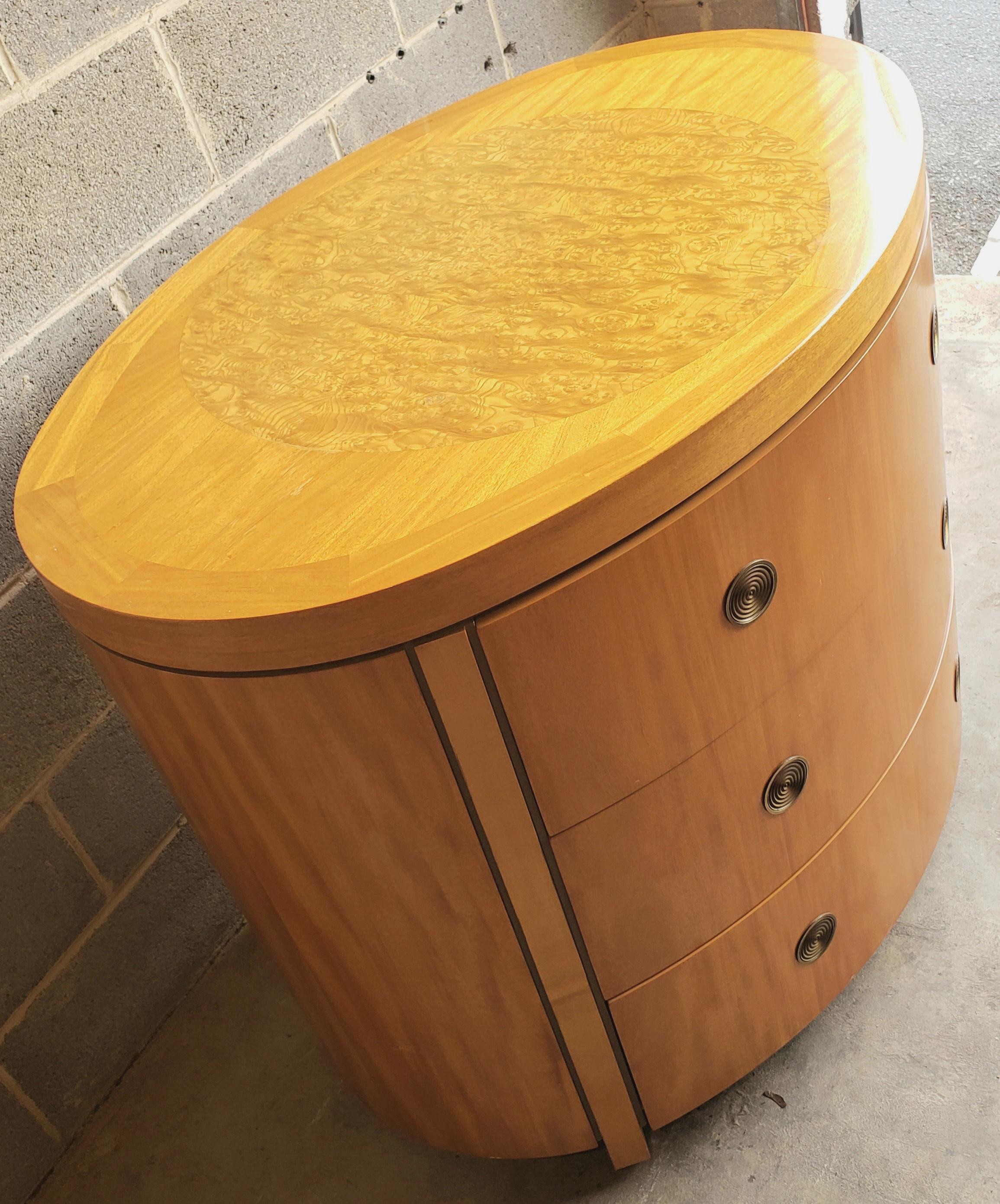 Charles Pfister for Baker prima vera mahogany three-drawer oval commode with satinwood banded and burl top.
Prima vera mahogany case and drawer fronts with flush concentric circled swiveling brass pulls. Four radius end legs and olive ash burled