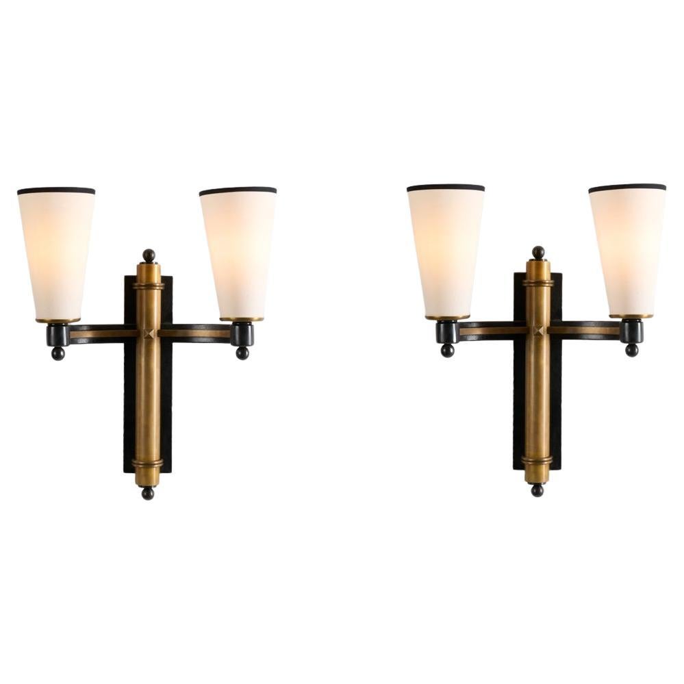This set of wall sconces by Charles Piguet possess a brooding allure: shaped in an elegant crisscross pattern, they feature a two-tone finish and arms that gently curve out, as in an embrace, from the wall on each side. With conical white shades