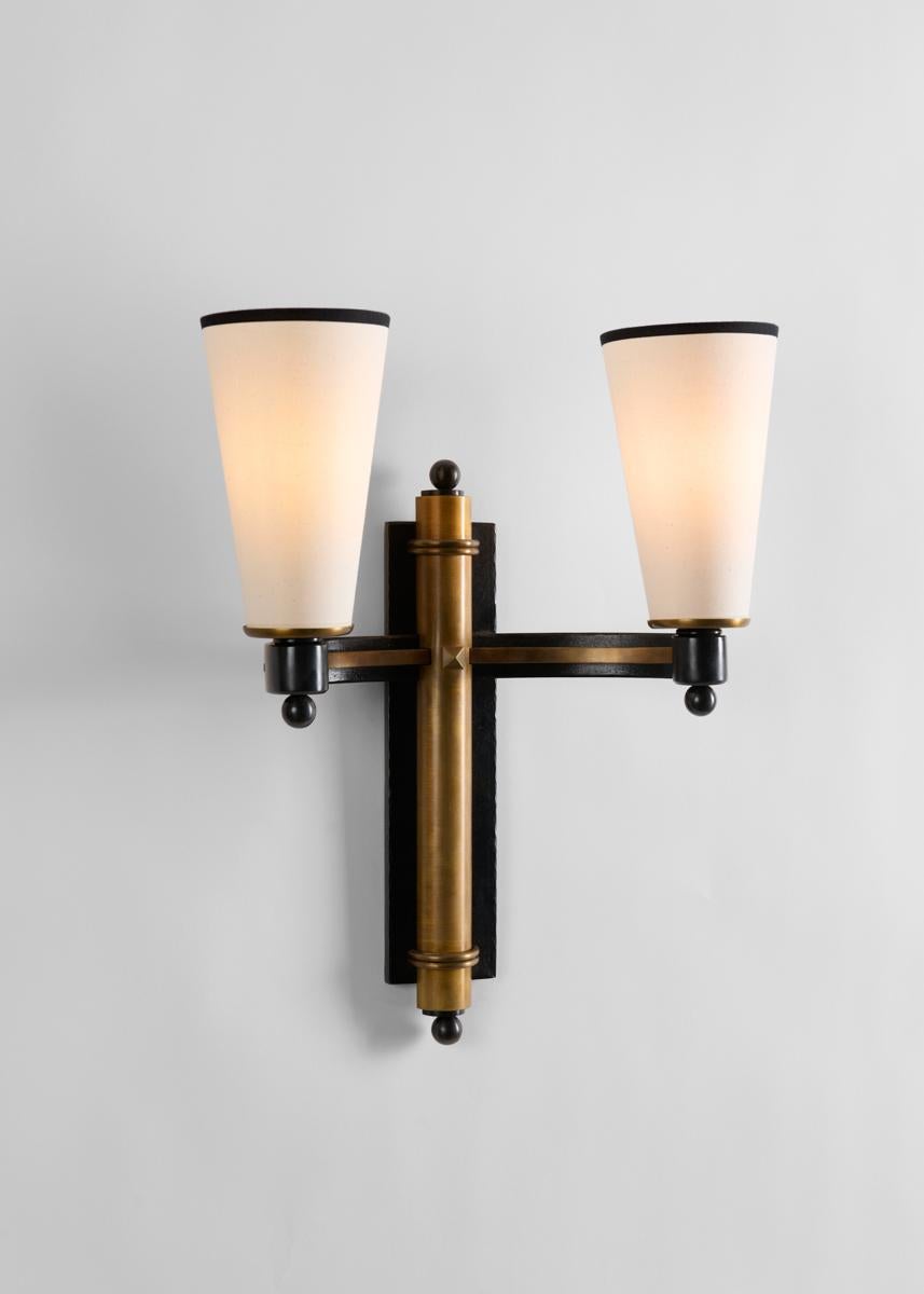 This pair of wall sconces by Charles Piguet possess a brooding allure: shaped in an elegant crisscross pattern, they feature a two-tone finish and arms that gently curve out, as in an embrace, from the wall on each side. With conical white shades