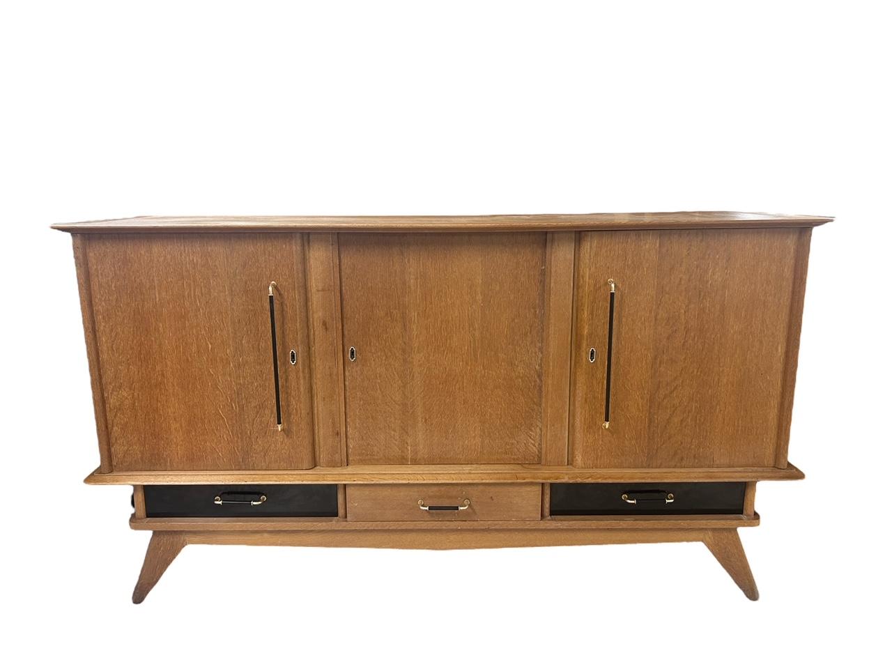 Rare modernist sideboard designed by Charles Ramos in the 1950's
Structure resting on four saber legs, with 6 hinged doors, three drawers under the doors in an alternation of ash and black laminate.
Handles in patinated brass.