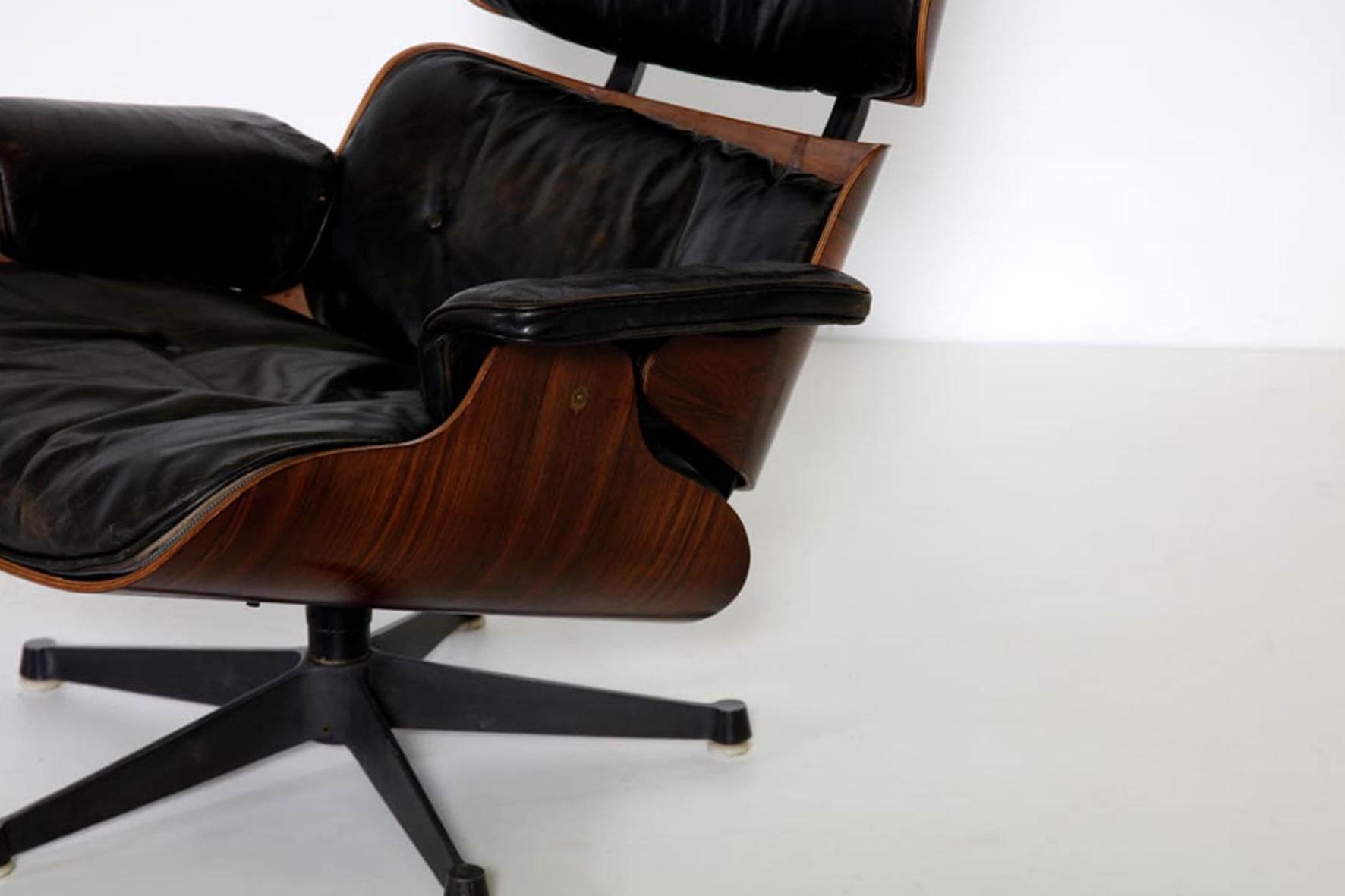 Iconic lounge chair with footrest designed by Charles and Ray Eames for Herman Miller production (1956).
The lounge chair and the footrest have a rosewood structure with the aluminium base covered in black leather. 
A swivel armchair, with a