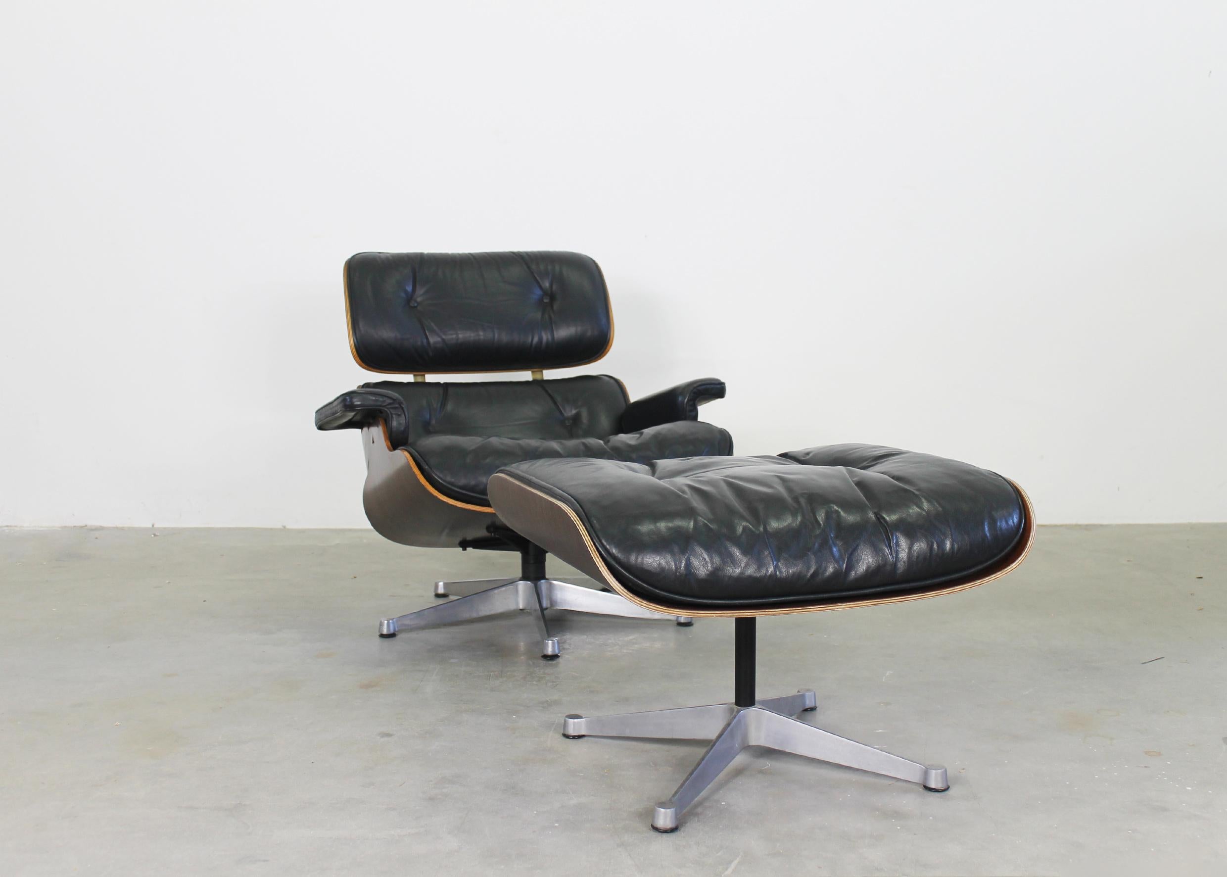 Lounge chair and ottoman with base in aluminum and steel, wooden shells filled with cushions in polyurethane foam covered with black leather. 
Both chair and ottoman were designed by Charles and Ray Eames in 1956 with the intention to create a chair