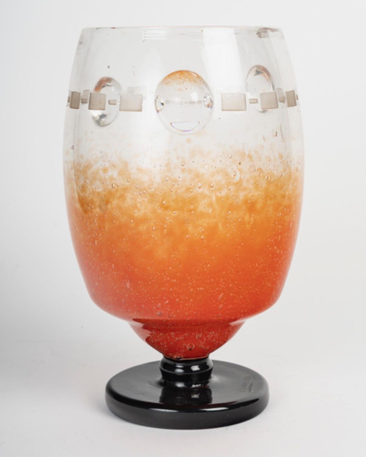 Charles Schneider (francese, 1881-1953)
Vaso su base a doccia in vetro incolore con forti bolle, colorazione intercalare con polveri arancioni fuse.
Base incollata a caldo in vetro nero.
Decorazioni geometriche incise all'acido e semisfere applicate