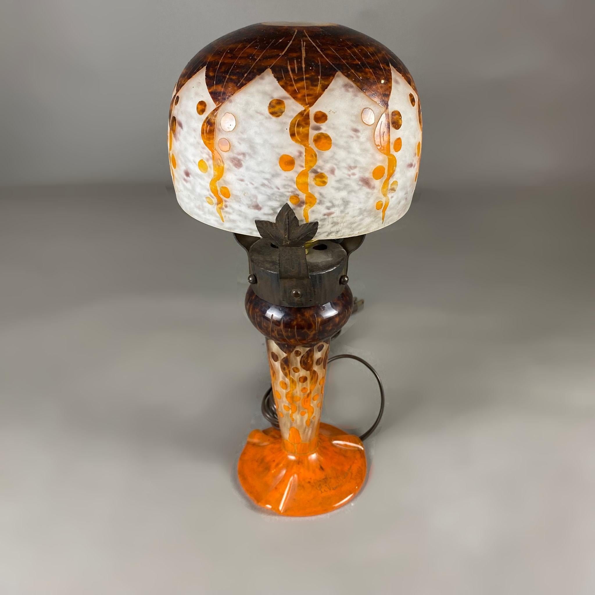 Lampe de table Rubaniers en verre camée et ferronnerie Le Verre Français des années 1920. La quincaillerie en fer rejoint les deux sections en verre camée de la lampe : l'écran supérieur en blanc, marron et orange et la base en orange et marron avec