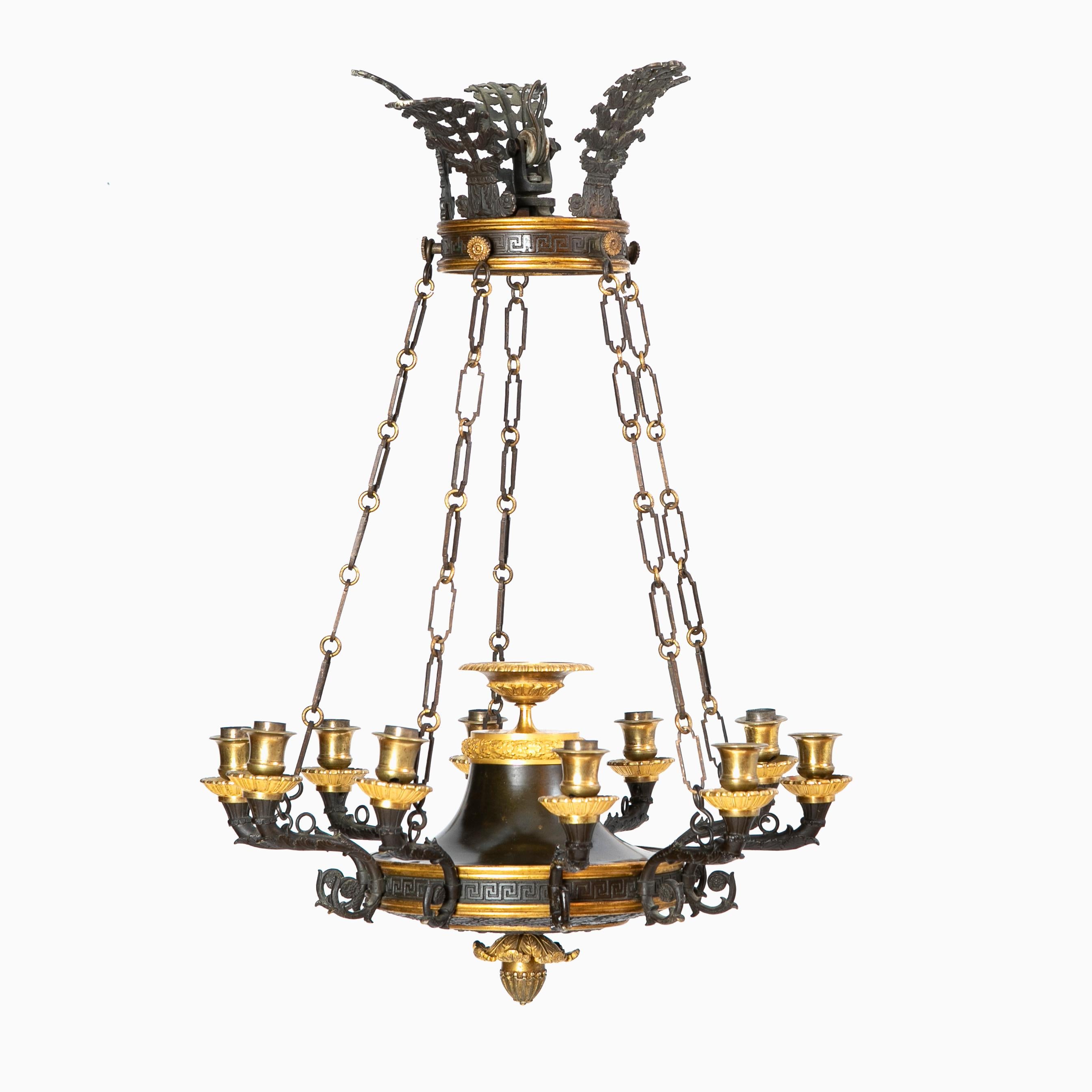 A French 10 arm Charles X chandelier in patinated bronze and ormolu.
Rich in details with a coronet adorned with à la grecque décor and a black polished leaf crown. Original chains supporting a circular bowl form ten light fixture, each adorned with