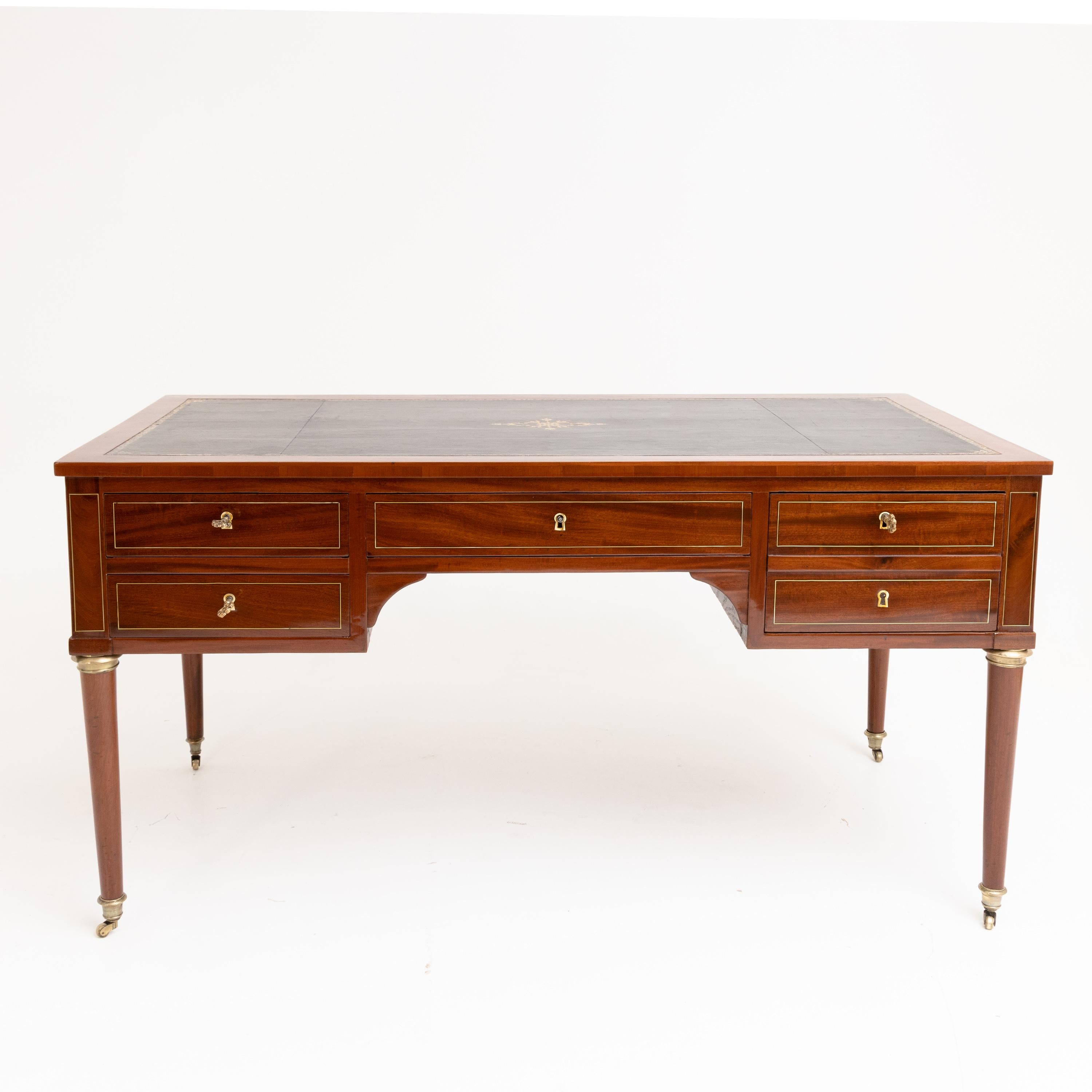 Bureau Plat on brass castors with conical legs and brass capitals. The front has four drawers with brass mouldings (one large drawer with compartments on the right) and pull-out surfaces on the sides. Like the surface, these are covered with