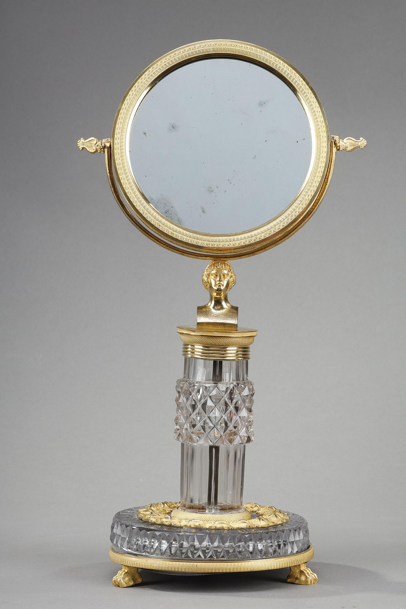 Charles X toilet mirror in cut crystal and gilt bronze. The circular mirror with its guilloché border is mounted on a rotating system attached to a diamond-tipped crystal shaft. The circular base with flower garland rests on claw feet. Work in the