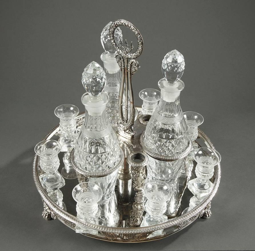 Early 19th century cut-crystal liqueur service composed of three decanters with their corks and seven glasses accented in crosspiece and diamond patterns. The silver plated tray with mirror is decorated with masks, swans and foliage. The central