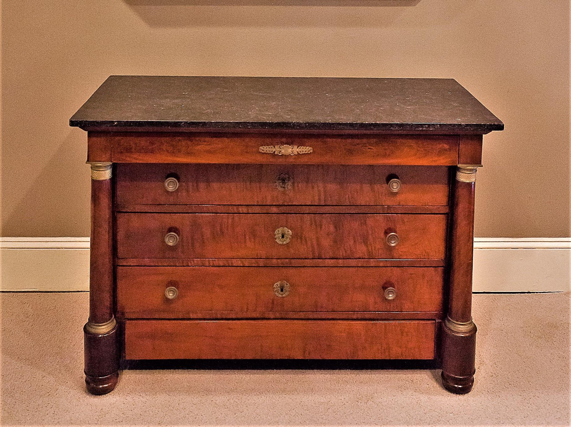 French polished mahogany and mahogany veneer with French oak secondary woods and a dark stone/marble top that appears to be original. Ormolu pulls and mounts, including on the freestanding columns. Bun feet. This commode/chest has five drawers