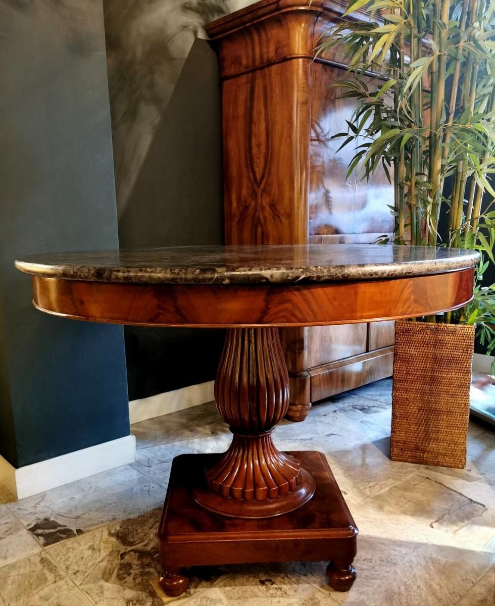 Massive mahogany round table with Emperador dark marble top, the solid square base with round legs supports a solid mahogany column with a refined and slender pod work; At the top of the column is fixed a sturdy cross that allows supporting the