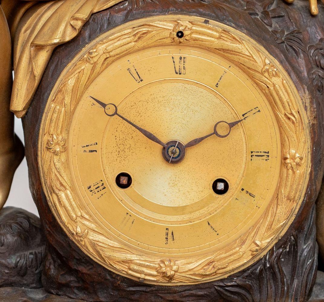 Charles X Gilt and Patinated Bronze Figural Clock, circa 1830, the circular dial with strike on bell movement, surmounted by Psyche sitting beside a pond, the rectangular base mounted with a central trophy of Cupid and attendant swans, with foliate