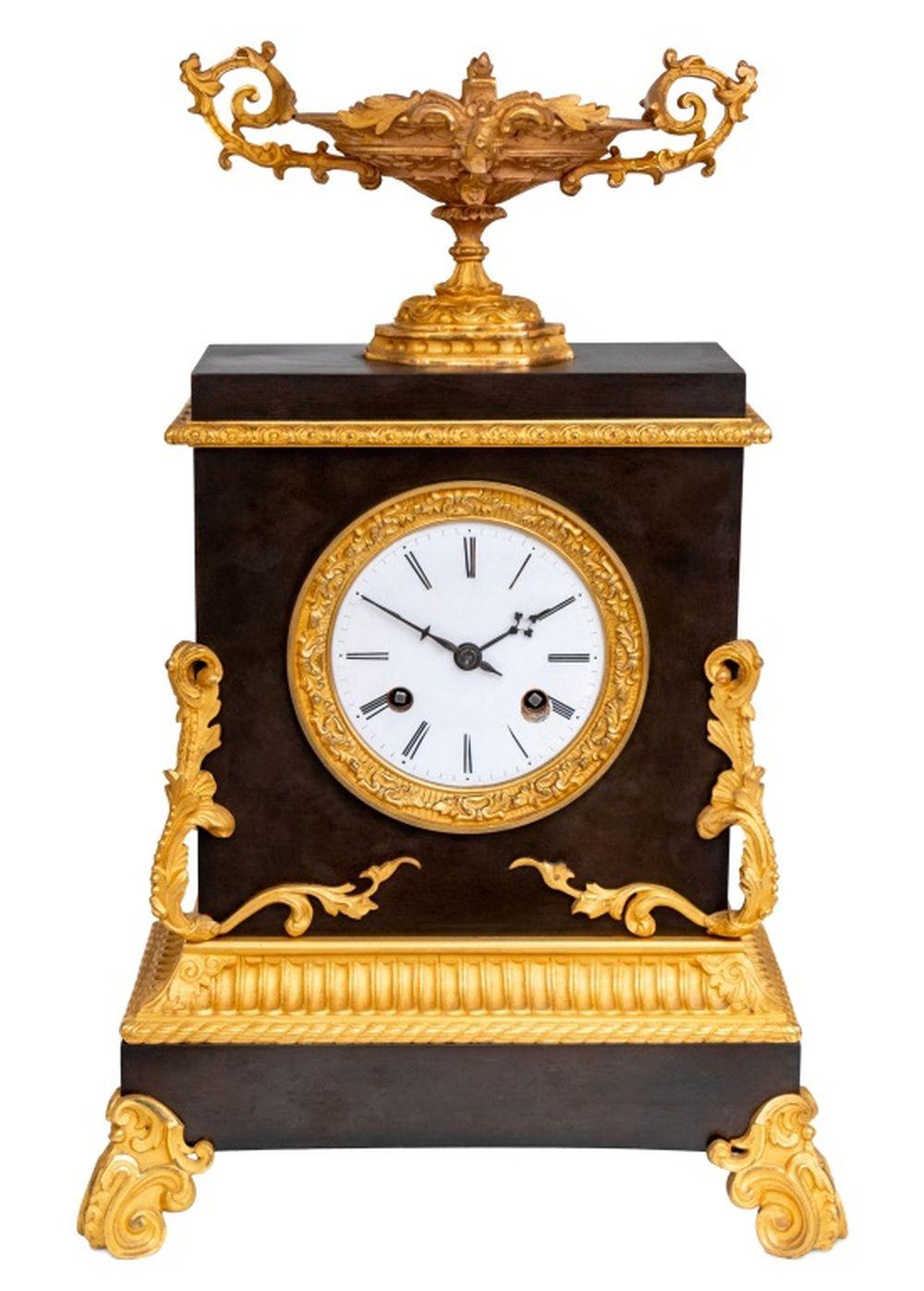 Charles X Gilt and Patinated Bronze Mantel Clock, circa 1830, with a circular enamel dial, the movement strike on bell, surmounted by a two handle tazza, acanthus scrolled mounts, and rectangular plinth on scrolled feet. 17