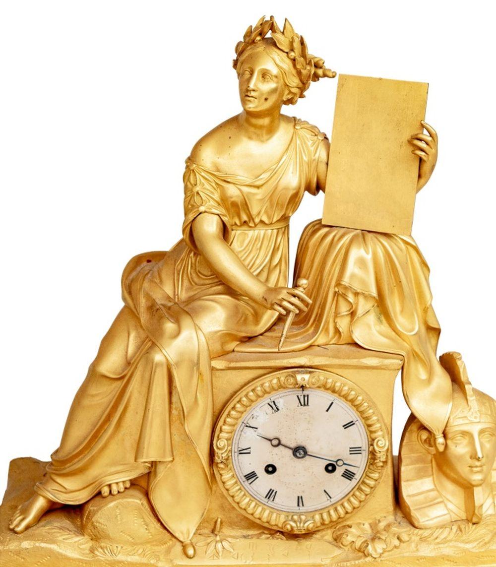 Pendule de cheminée figurative en bronze doré Charles X, vers 1830, le cadran argenté avec mouvement à sonnerie, surmonté d'une figure assise de Cléopâtre écrivant à Marc Antoine, sur une base rectangulaire ornée de trophées et de couronnes de