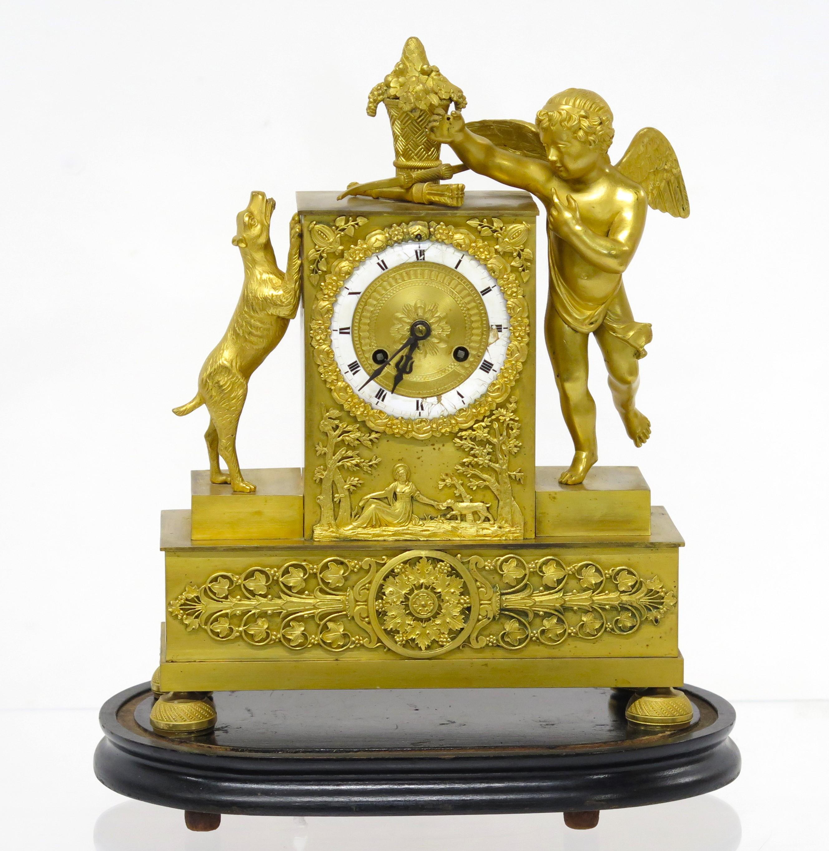 a Charles X gilt bronze mantel clock with Cupid and a dog on its hind legs barking / jumping / or begging, the figures flank the rectangular clock, the dog appears to be trying to get the basket on top of the clock, Cupid may be missing something
